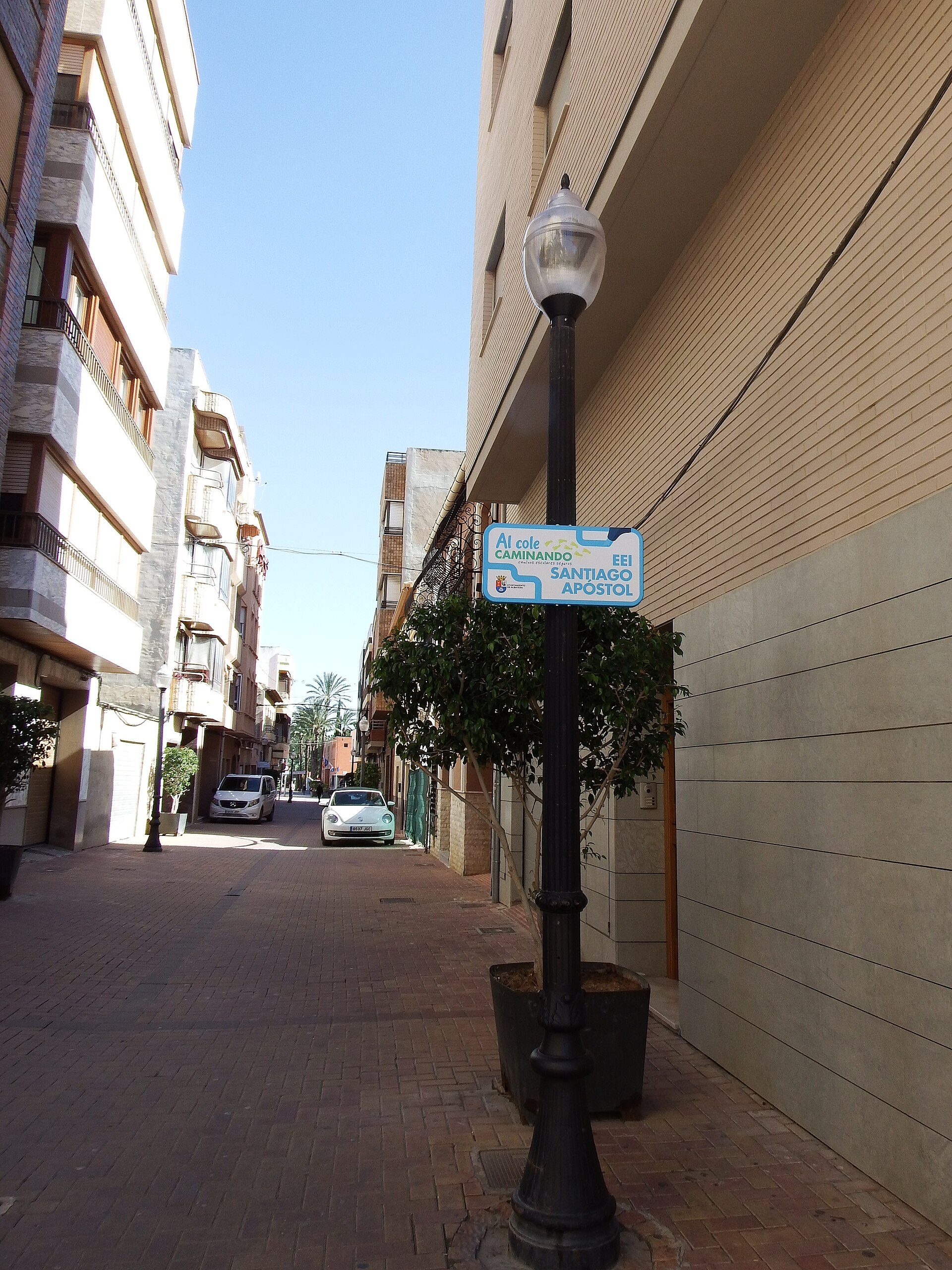 Alt text: Narrow street with modern buildings, clear blue sky, and a street sign.