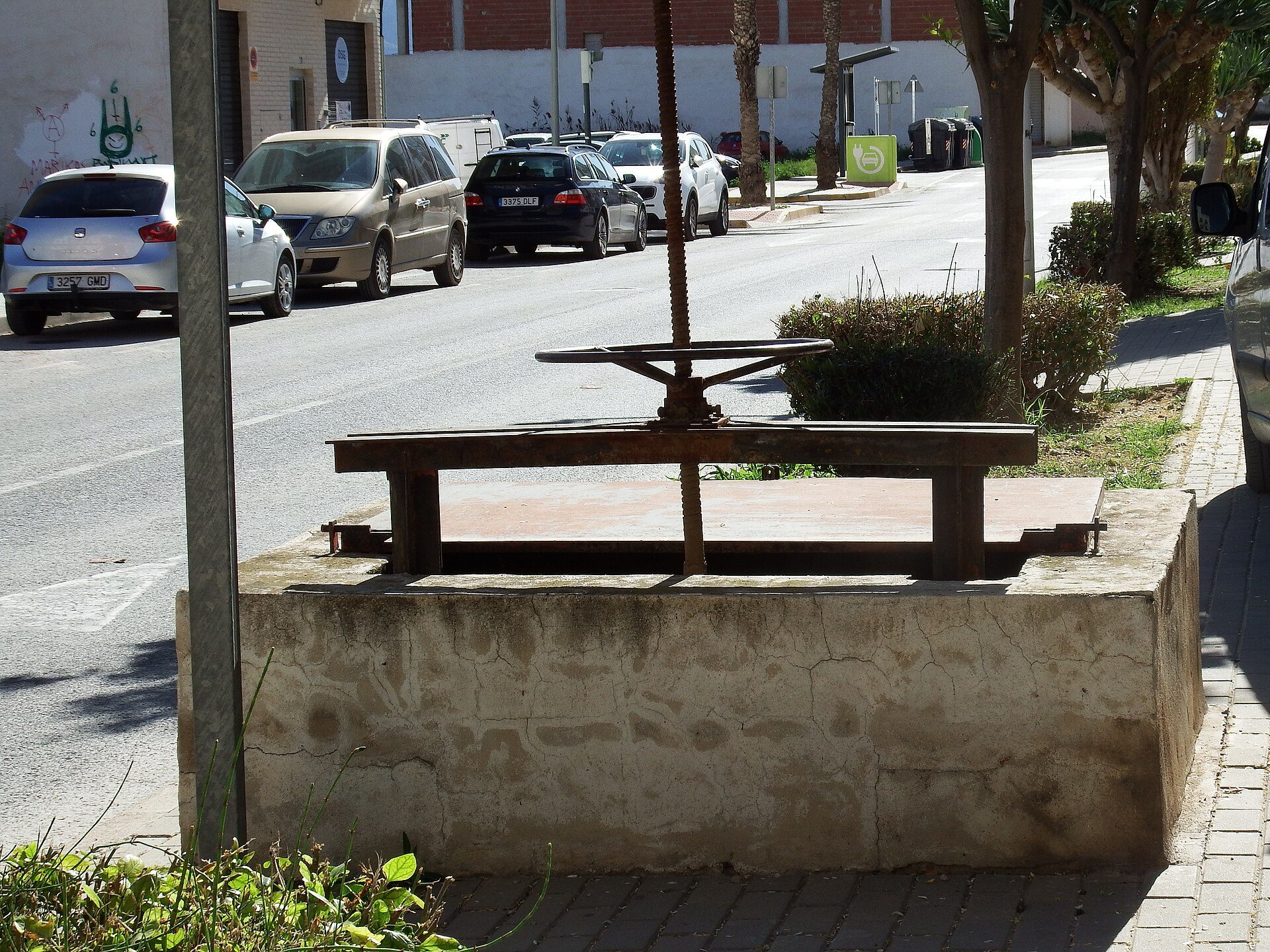 A wooden bench with a metal structure, situated on a sidewalk next to a street.