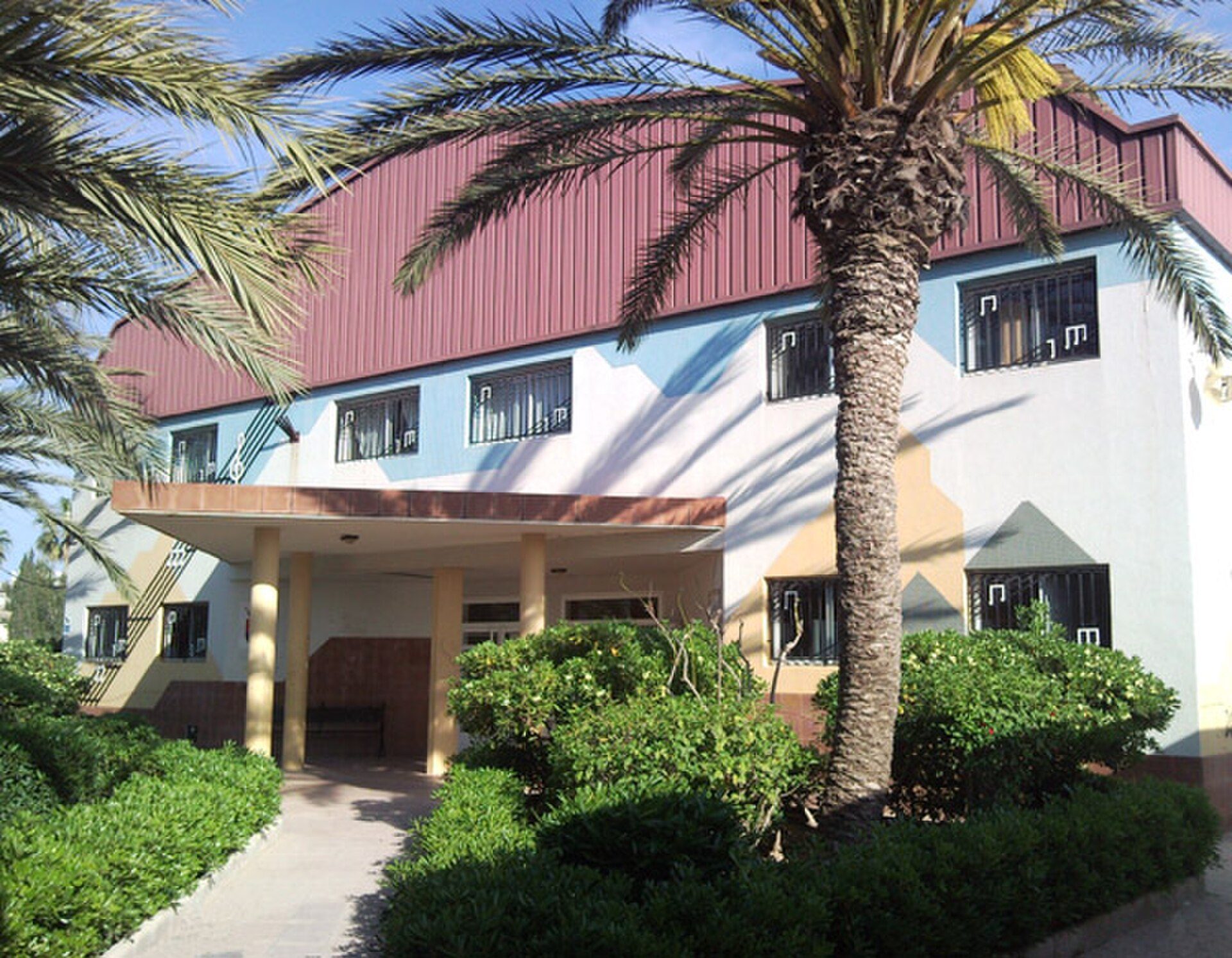 Two-story building with balconies, palm trees, and a well-maintained garden.