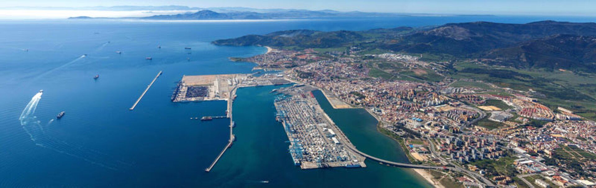Aerial view of a coastal city with a large harbor and surrounding mountains.