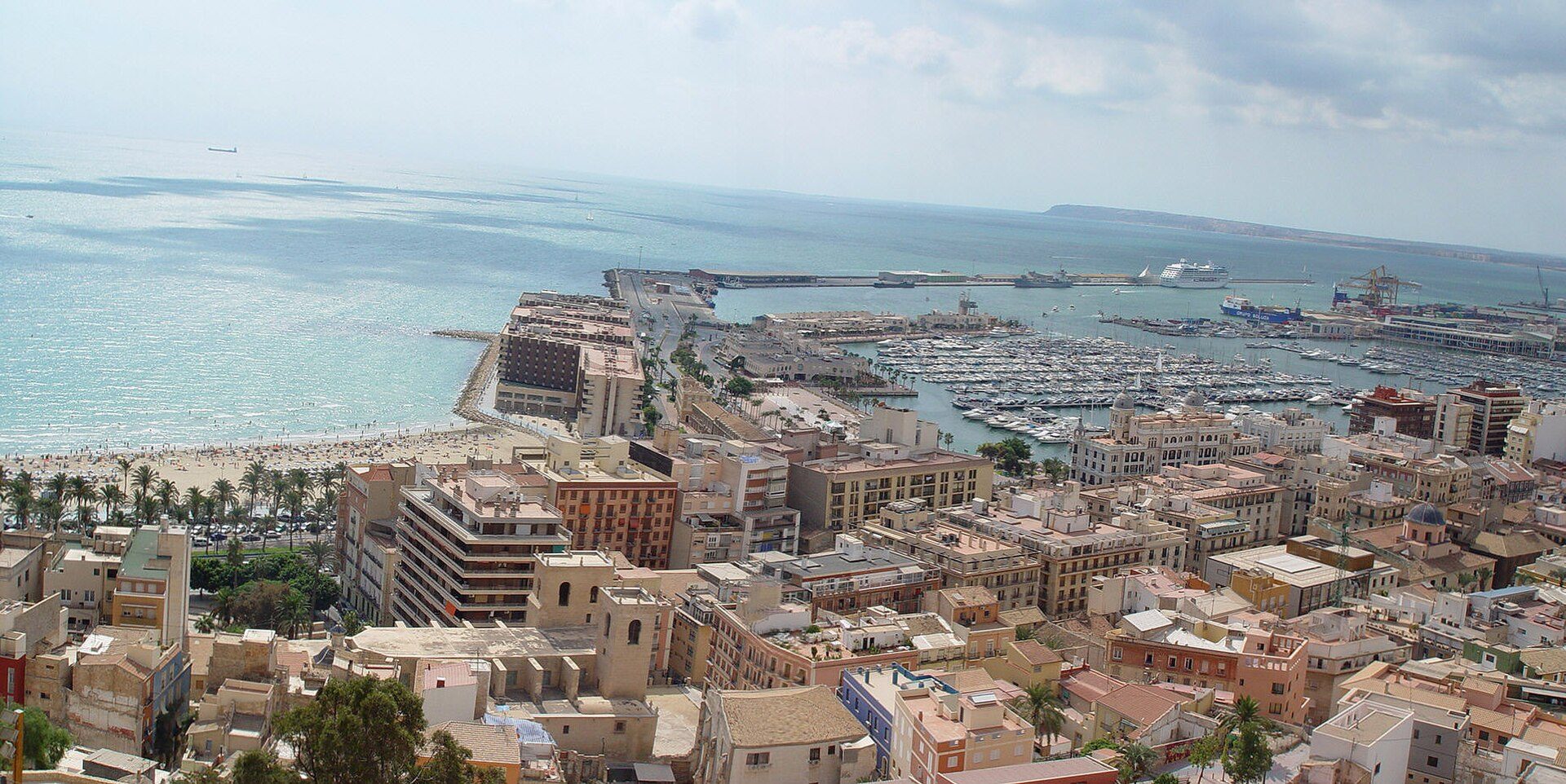 Coastal cityscape with sea view, modern apartment, balcony, beach, marina, and cruise ship.