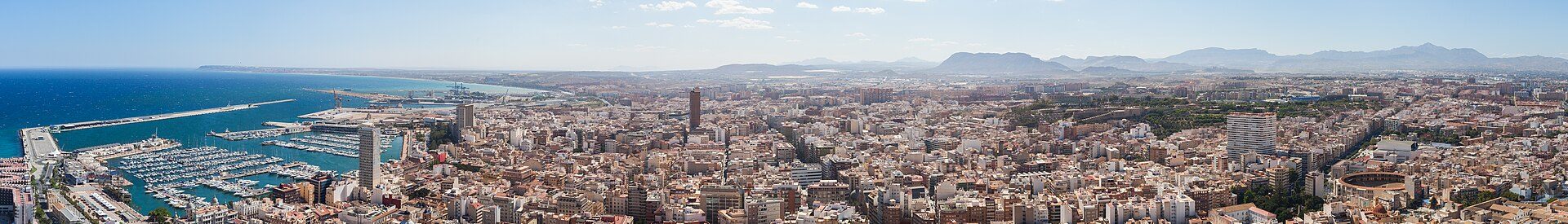 Aerial view of a coastal city with a marina and mountainous backdrop.