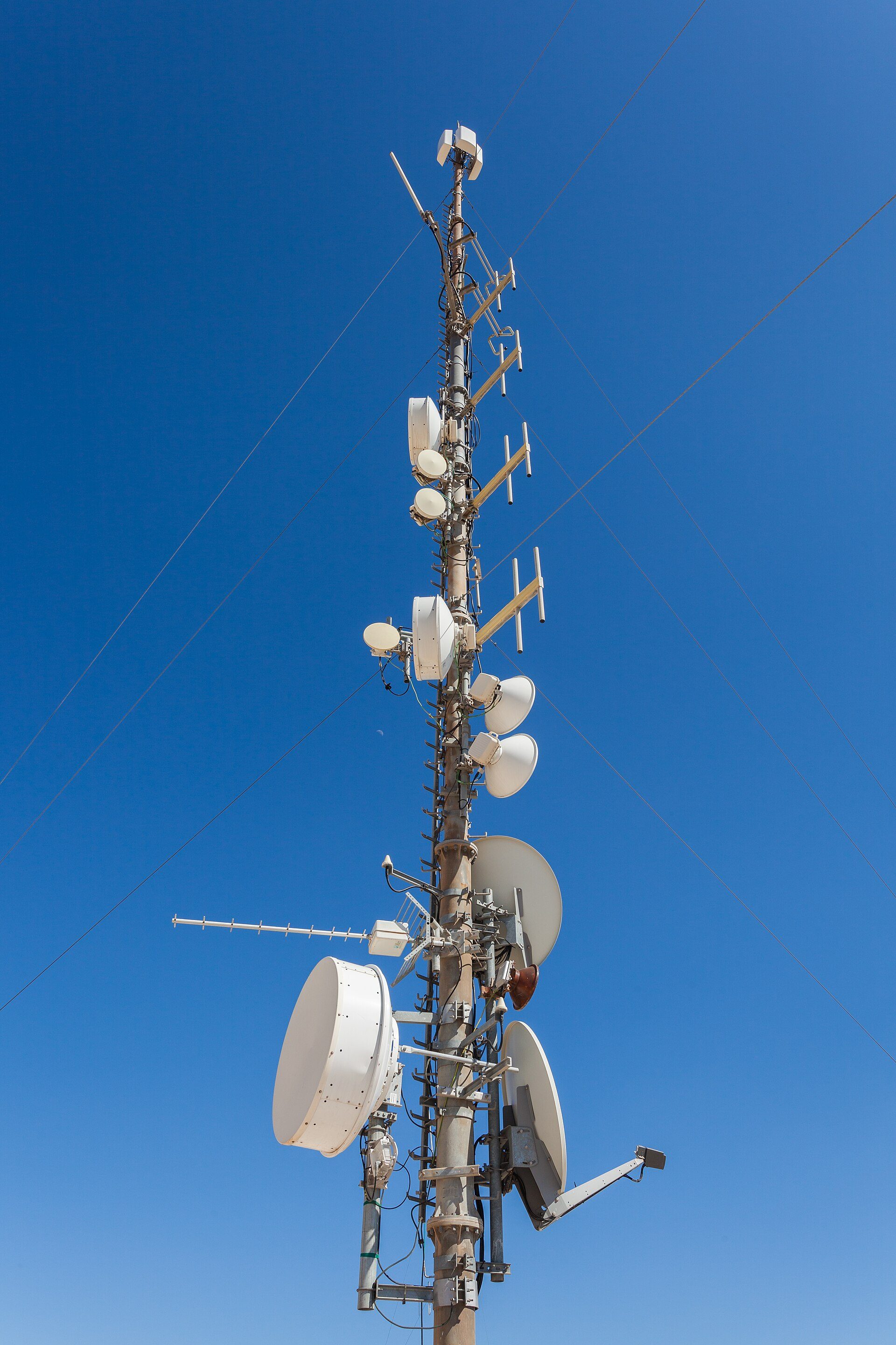 A tall telecommunications tower with various antennas and dishes against a clear blue sky.