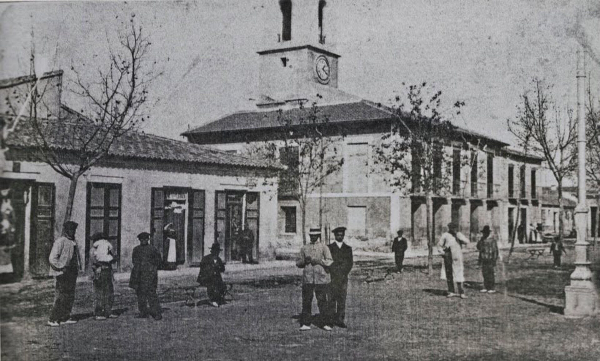 Historic building with clock tower, surrounded by people, in a courtyard setting.