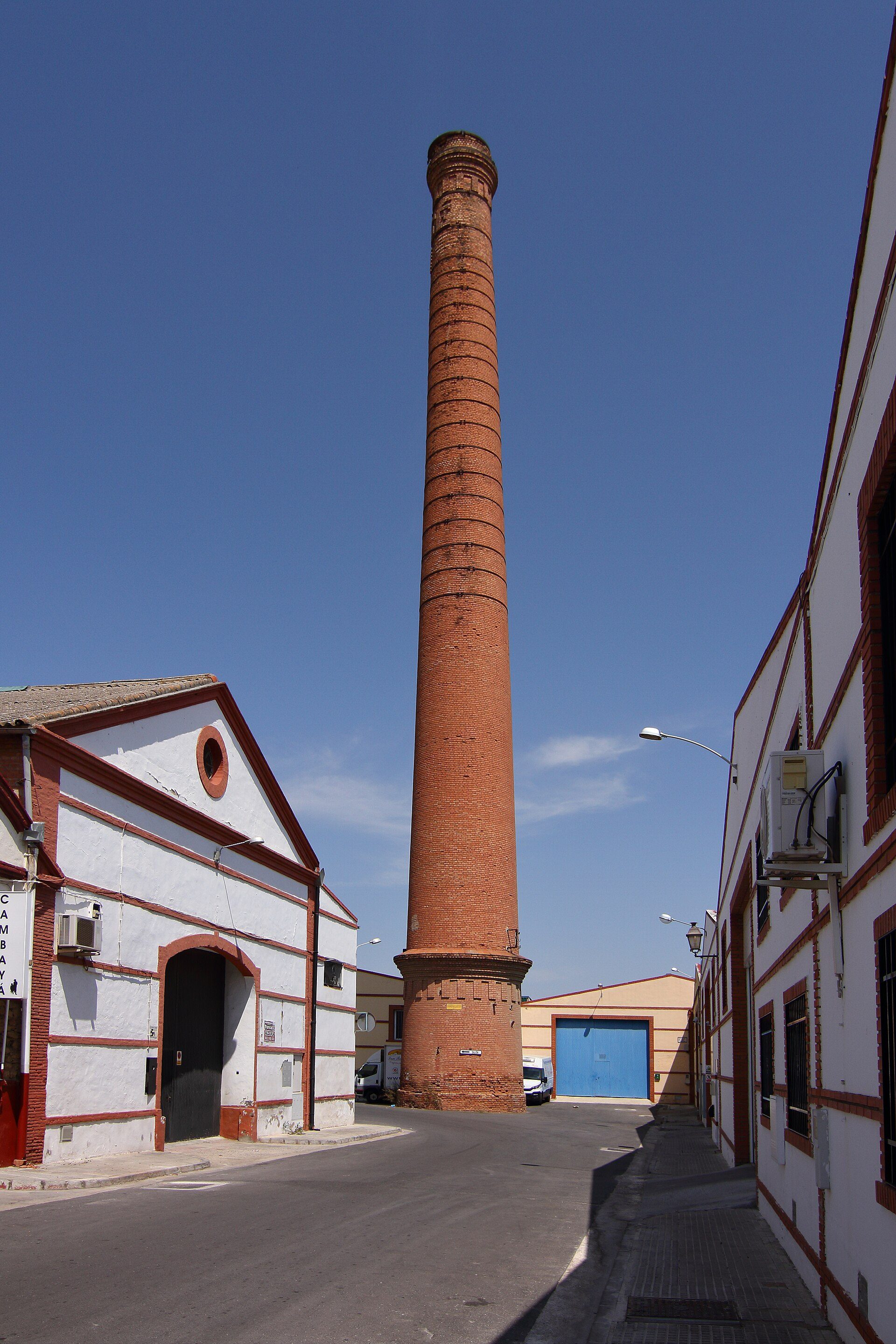 Alt text: Brick chimney, white building with red trim, clear blue sky.
