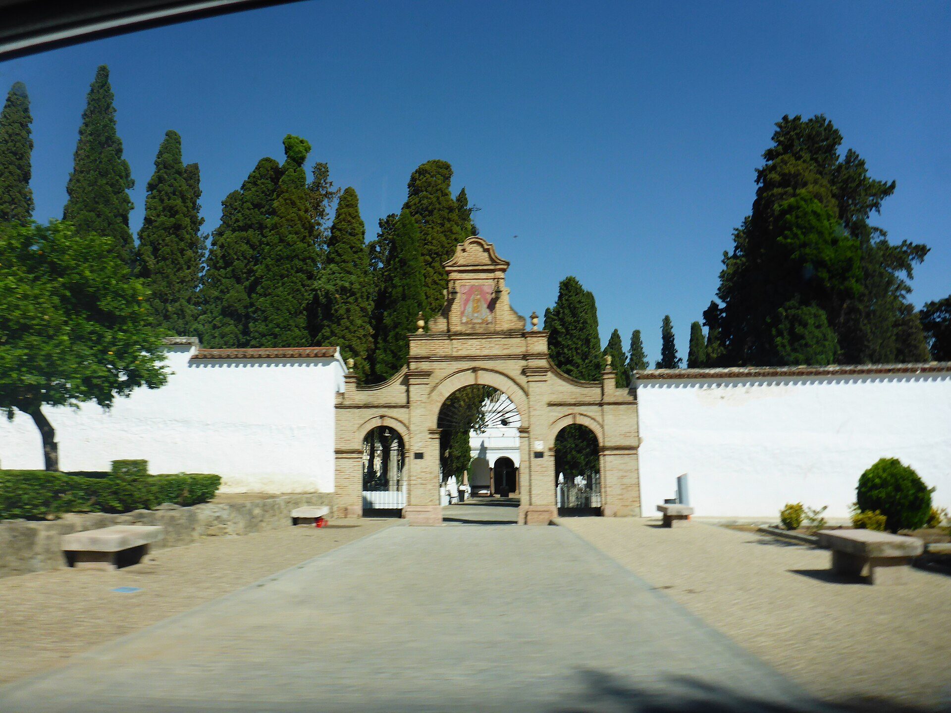 Alt text: Courtyard view with archway, white walls, and tall trees.