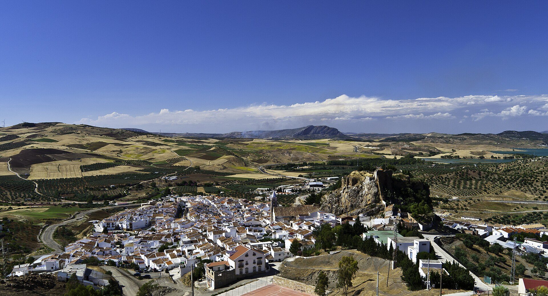 Alt text: Panoramic view of a quaint village with white buildings, rolling hills, and a clear blue sky.