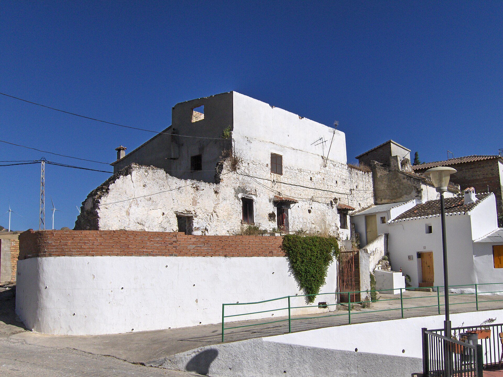 Old white building with brick base, small windows, and a clear blue sky view.