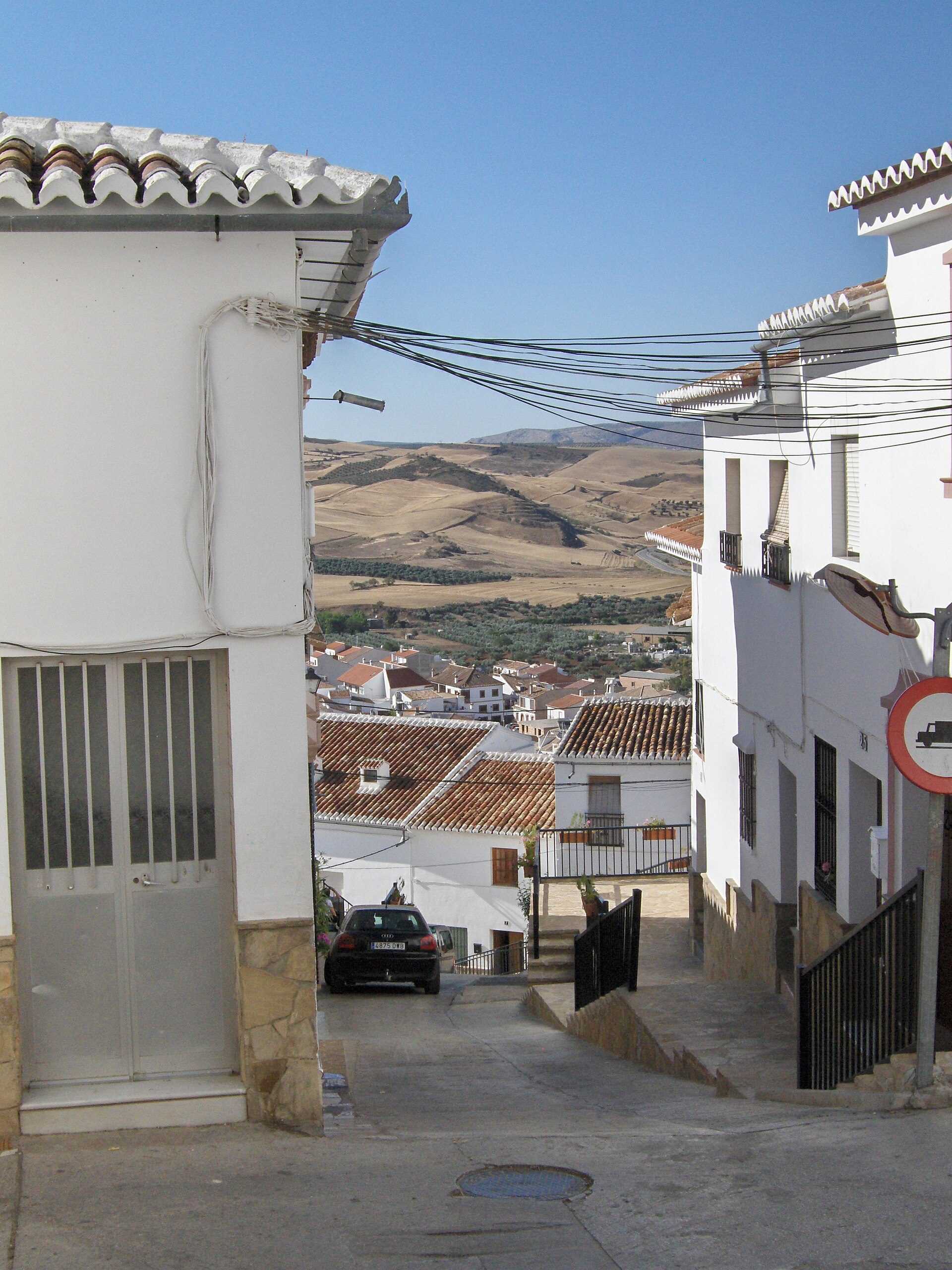 White house with red-tiled roof, narrow street, scenic hillside view.