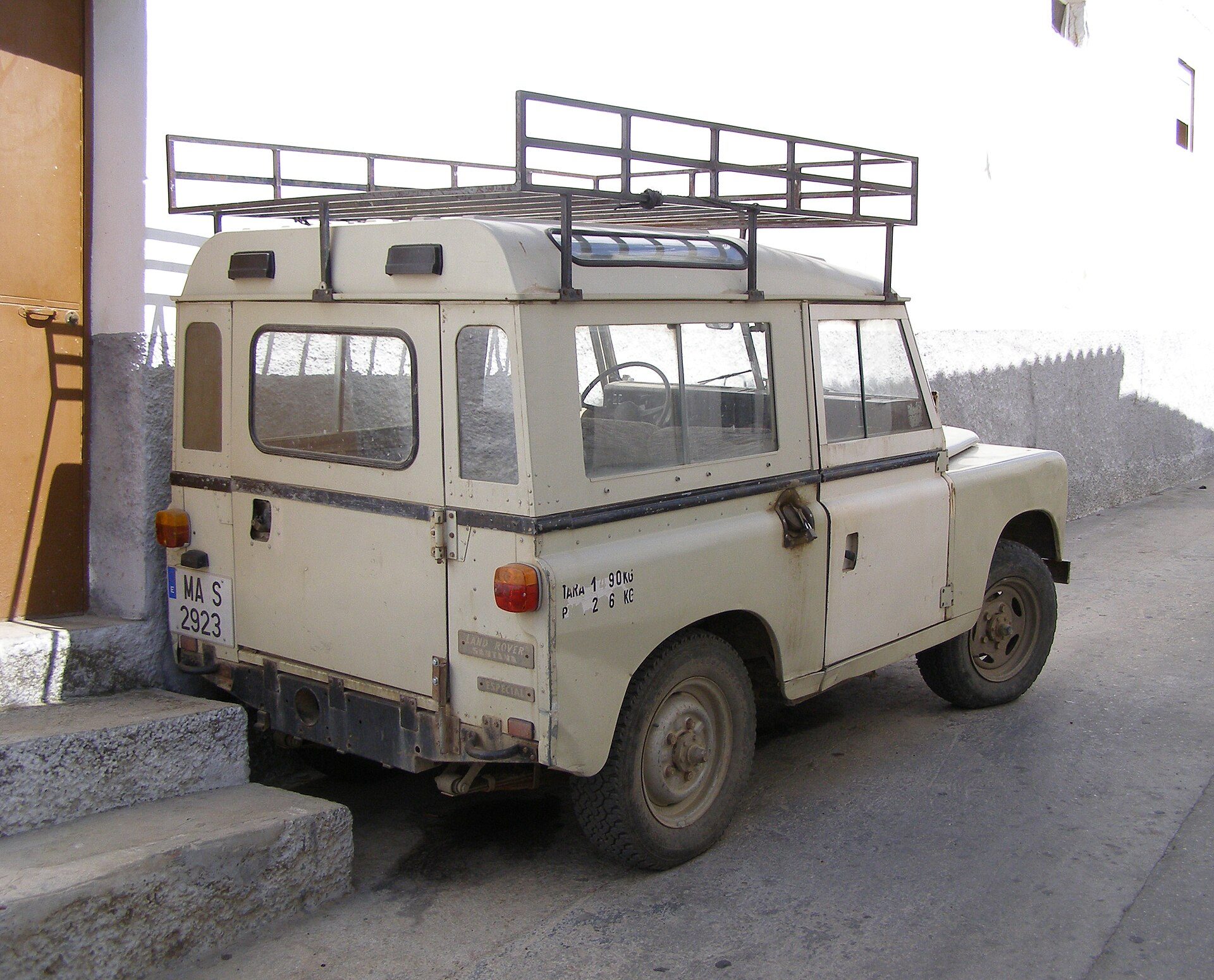Old beige SUV with roof rack parked on a concrete surface.