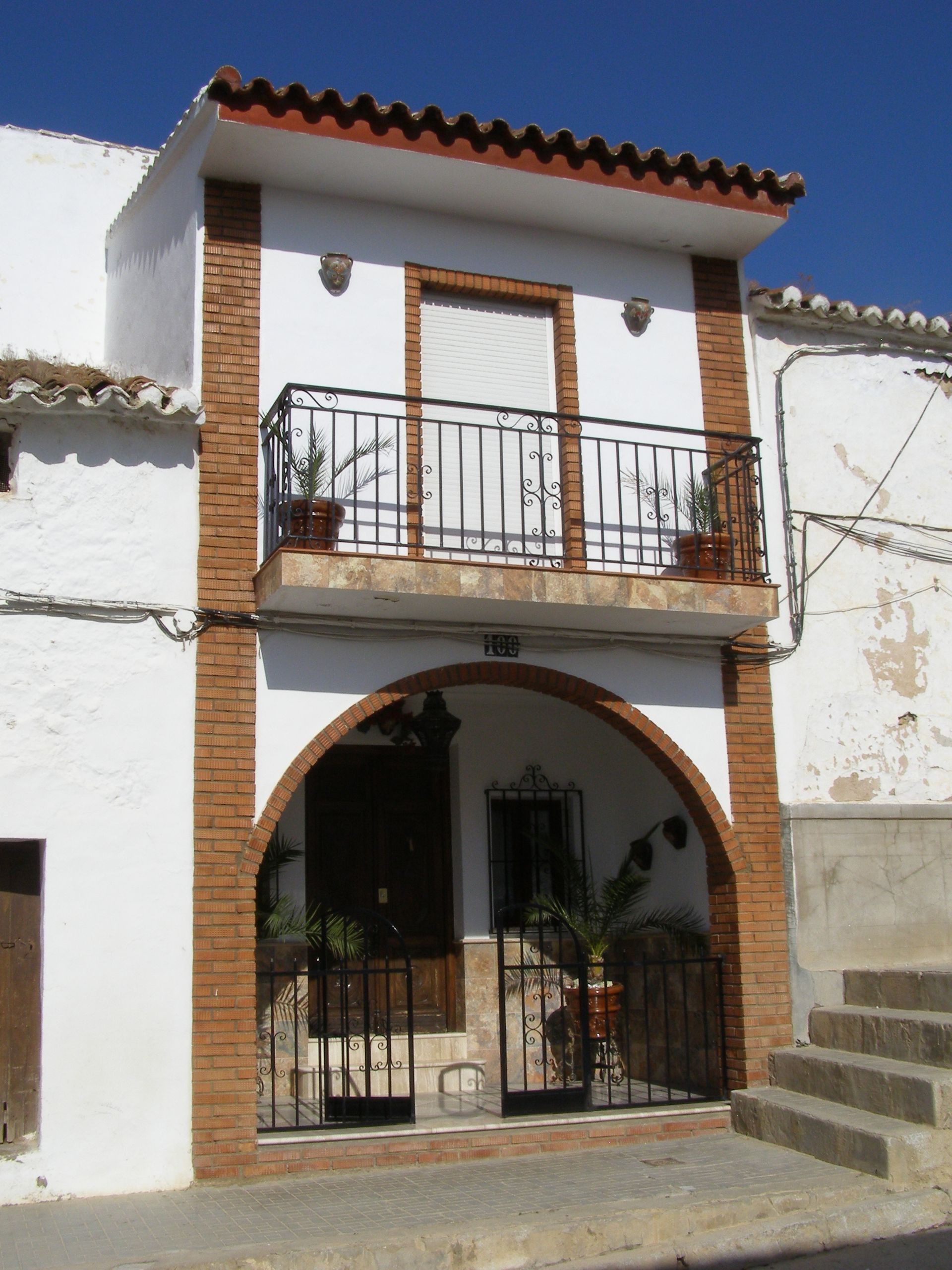 Two-story house with balcony, arched entrance, and potted plants.