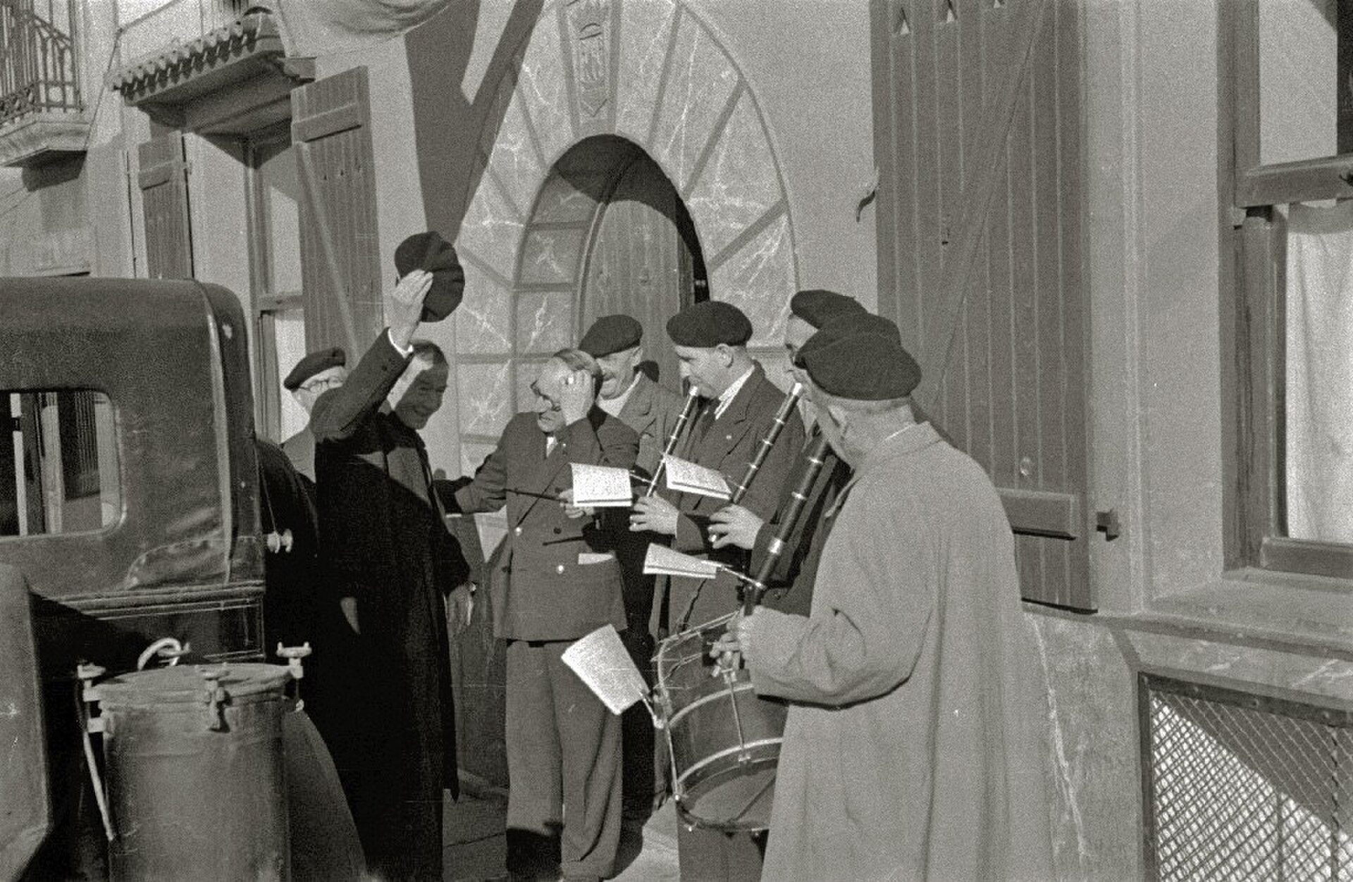 A black and white photo of a group of people, some in military uniforms, gathered outside a building.