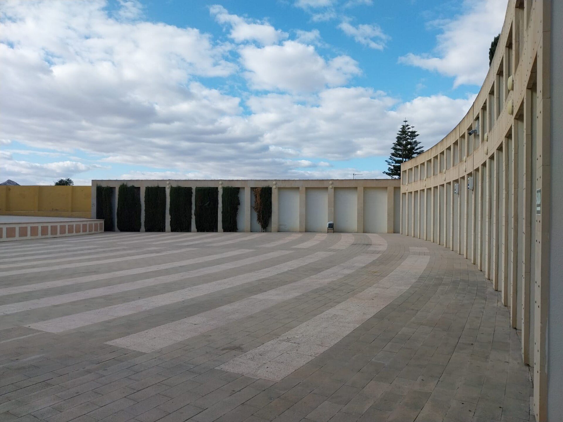 Outdoor patio with curved wall, paved flooring, and a view of the sky.