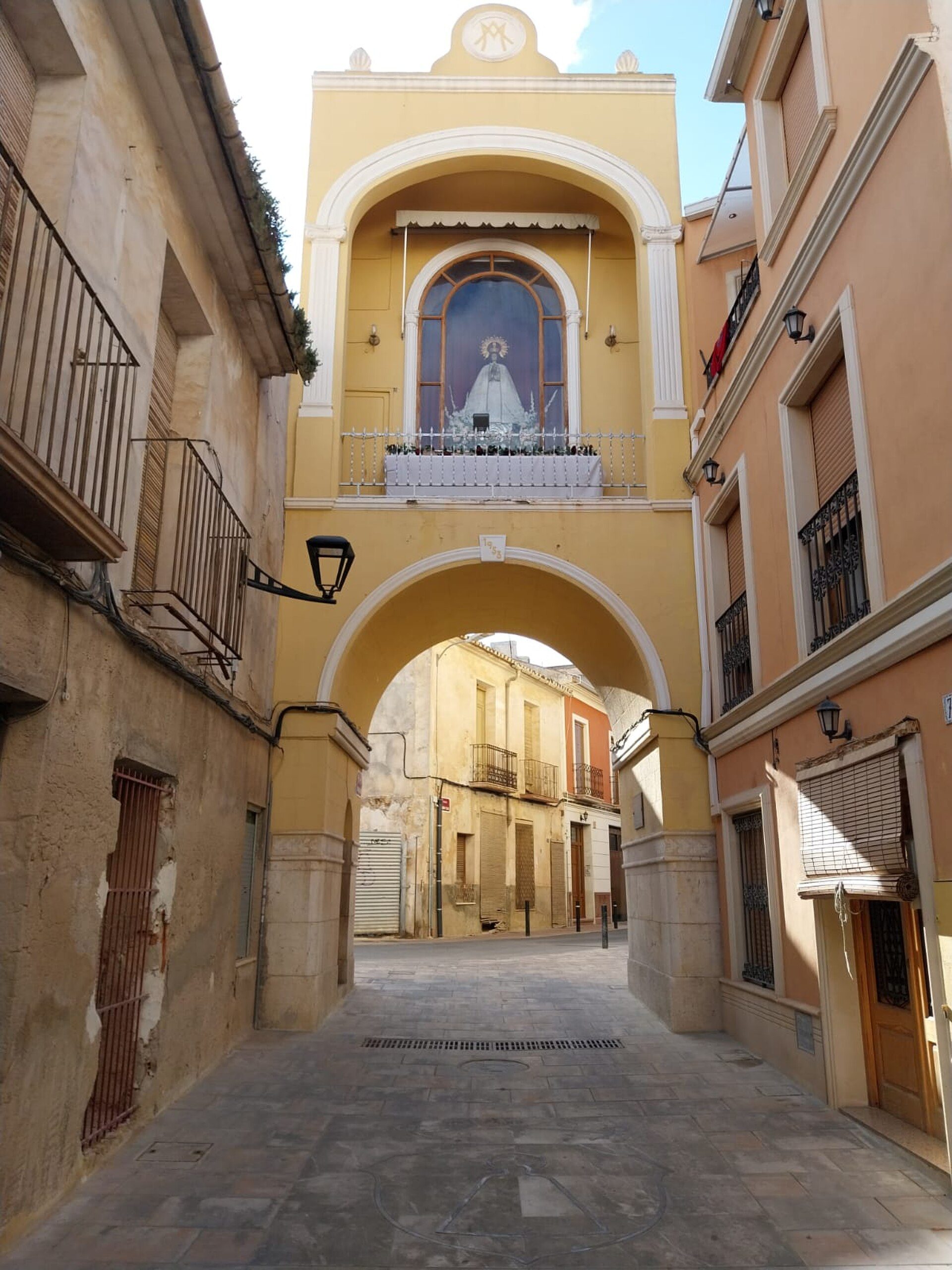 Alt text: Narrow alley with arched passageway, balconies, and a statue view.