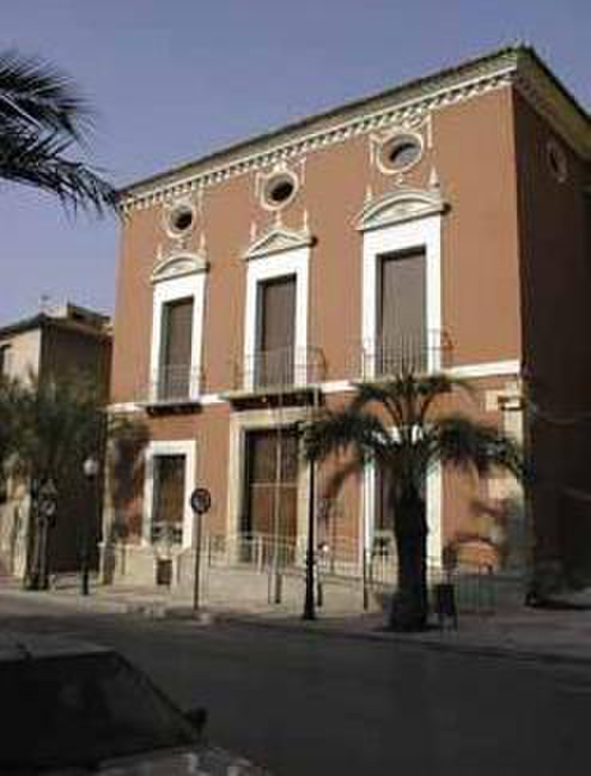 A three-story building with balconies, large windows, and a palm tree view.