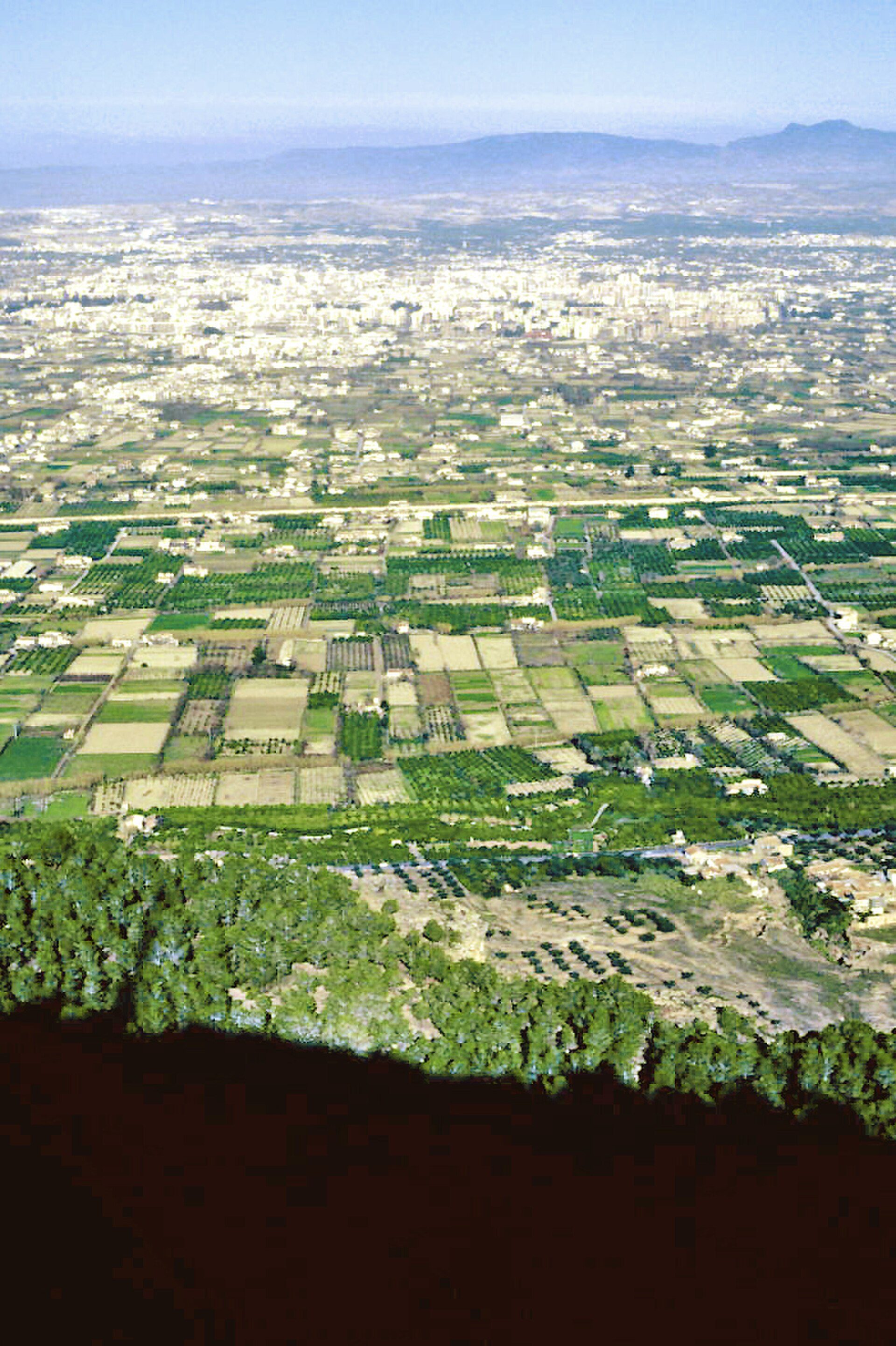 Aerial view of cityscape and agricultural fields with distant mountains.