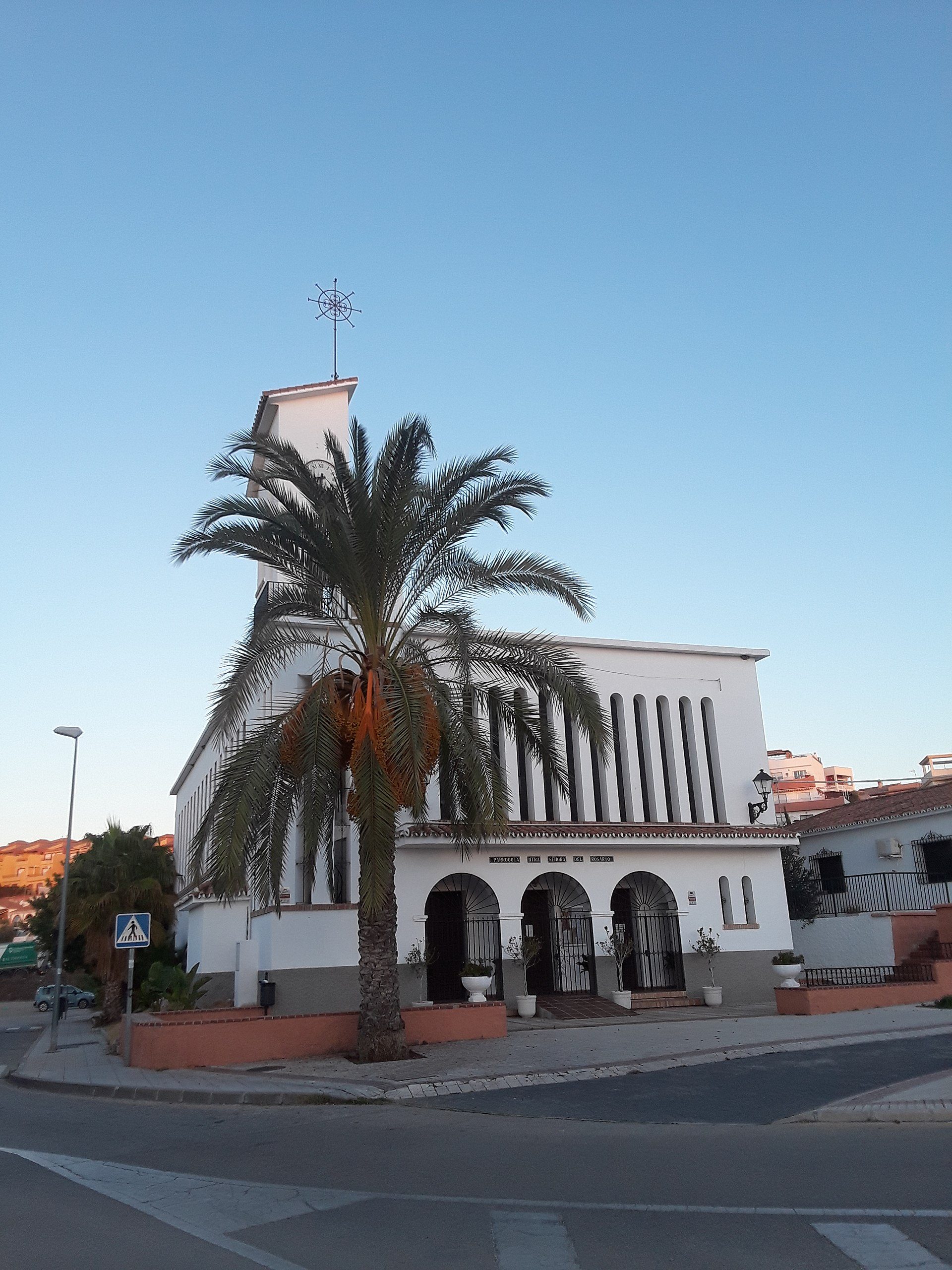 White building with palm tree, street view, arched entrance, clear blue sky.