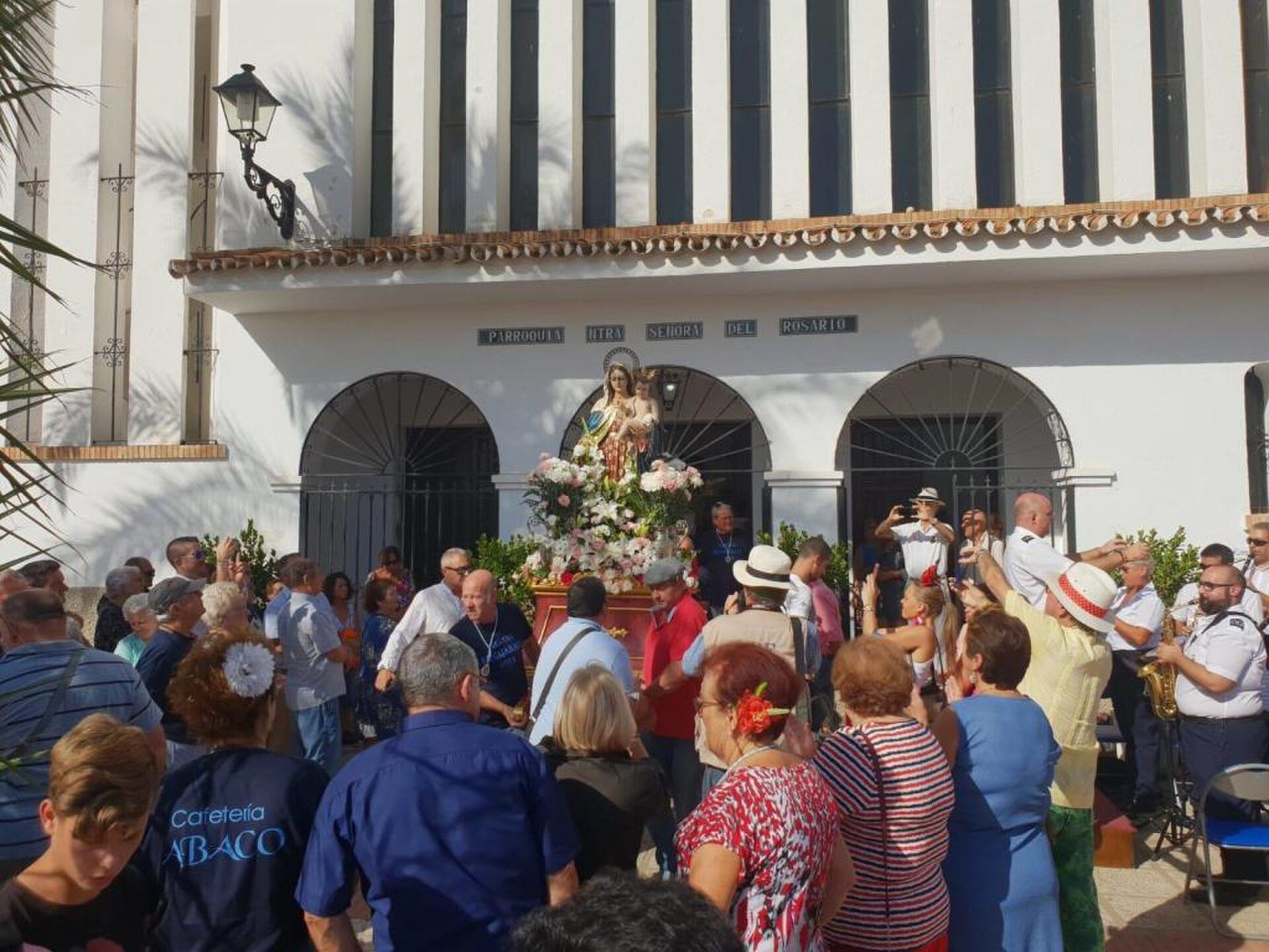 Alt text: Outdoor gathering in front of a white building with arched entrances and a statue.