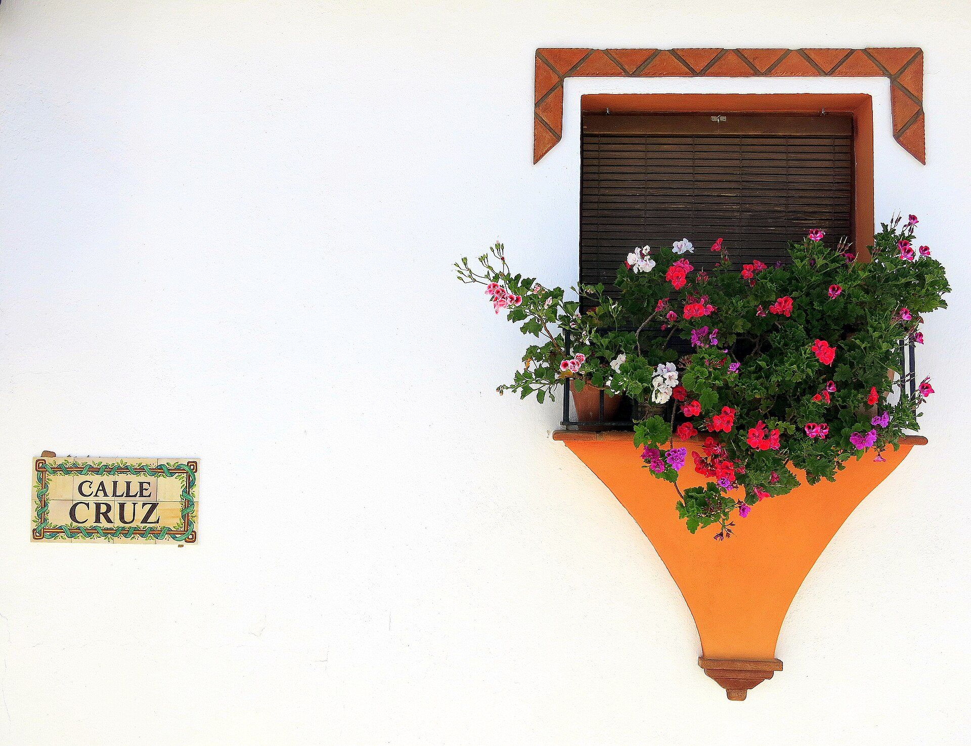 Alt text: White-walled room with a flower-filled window box and a "Calle Cruz" street sign.