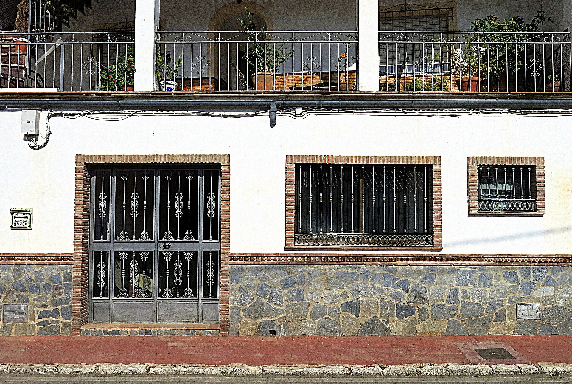 A two-story building with a balcony, stone base, and barred windows.