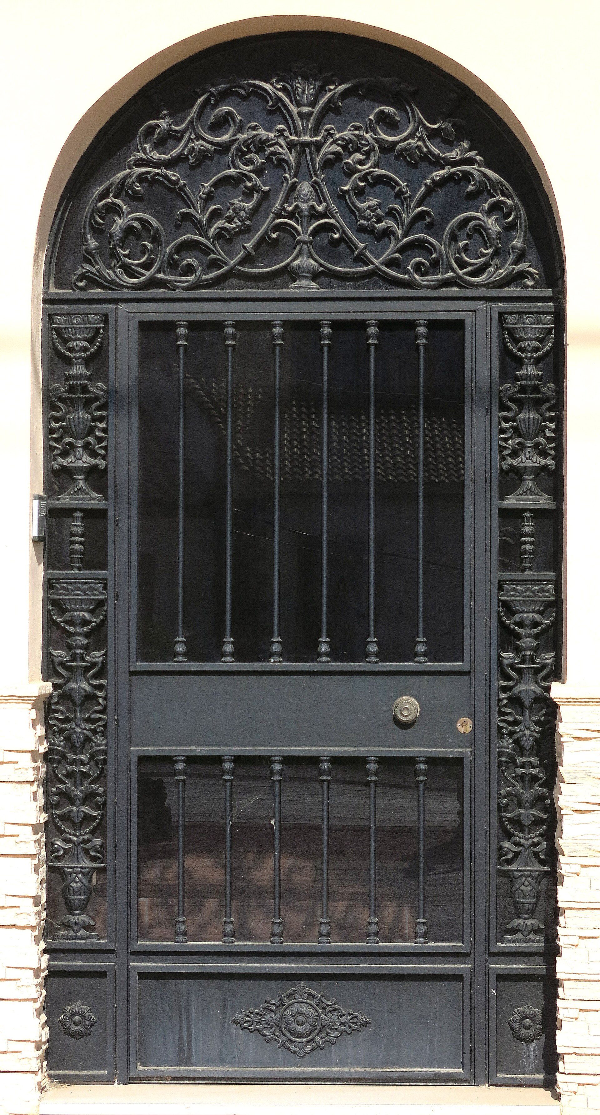 Elegant black wrought iron door with intricate designs and a small window.