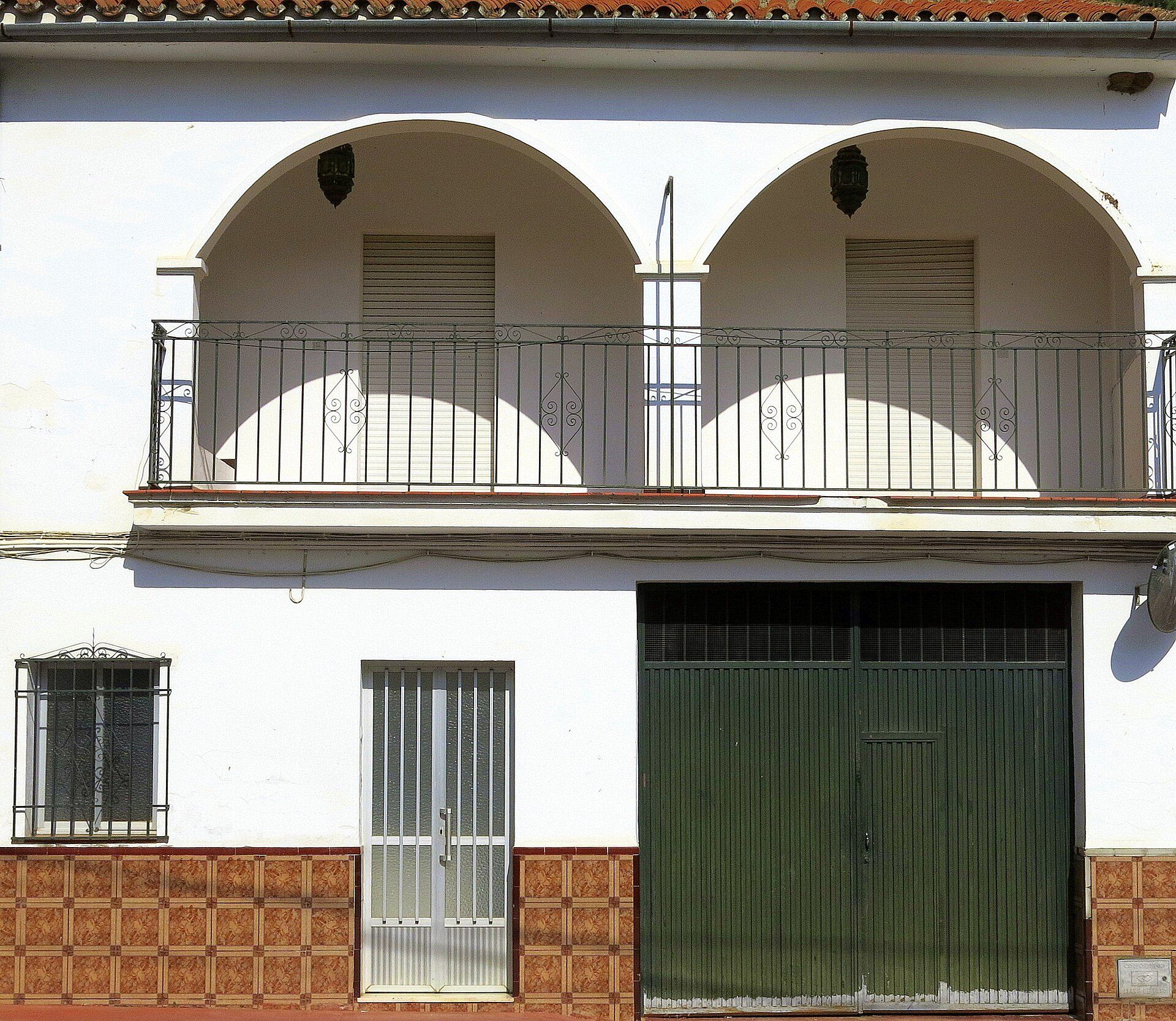 Two-story building with arched balcony, white walls, and a green garage door.