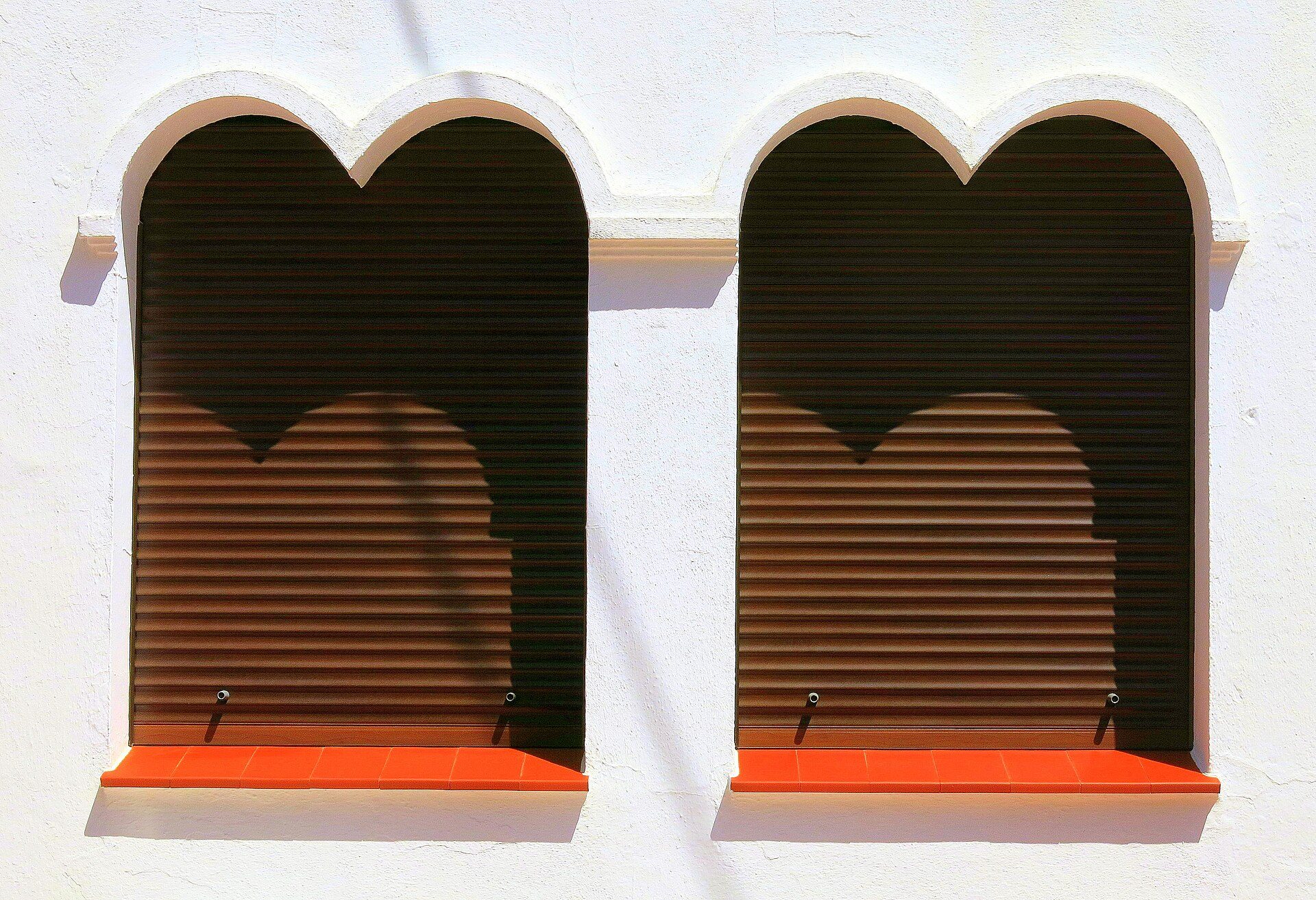 Two arched windows with brown blinds and orange sills on a white wall.
