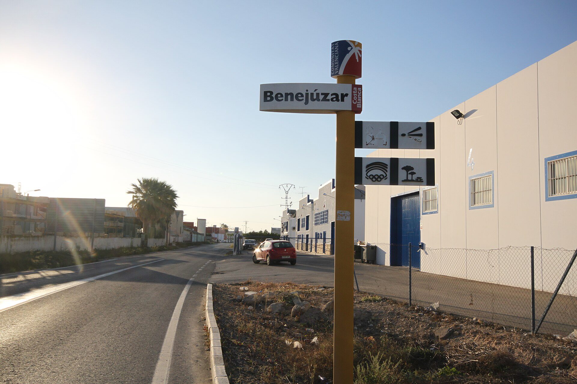 A street view with a signpost, palm trees, and a clear blue sky.