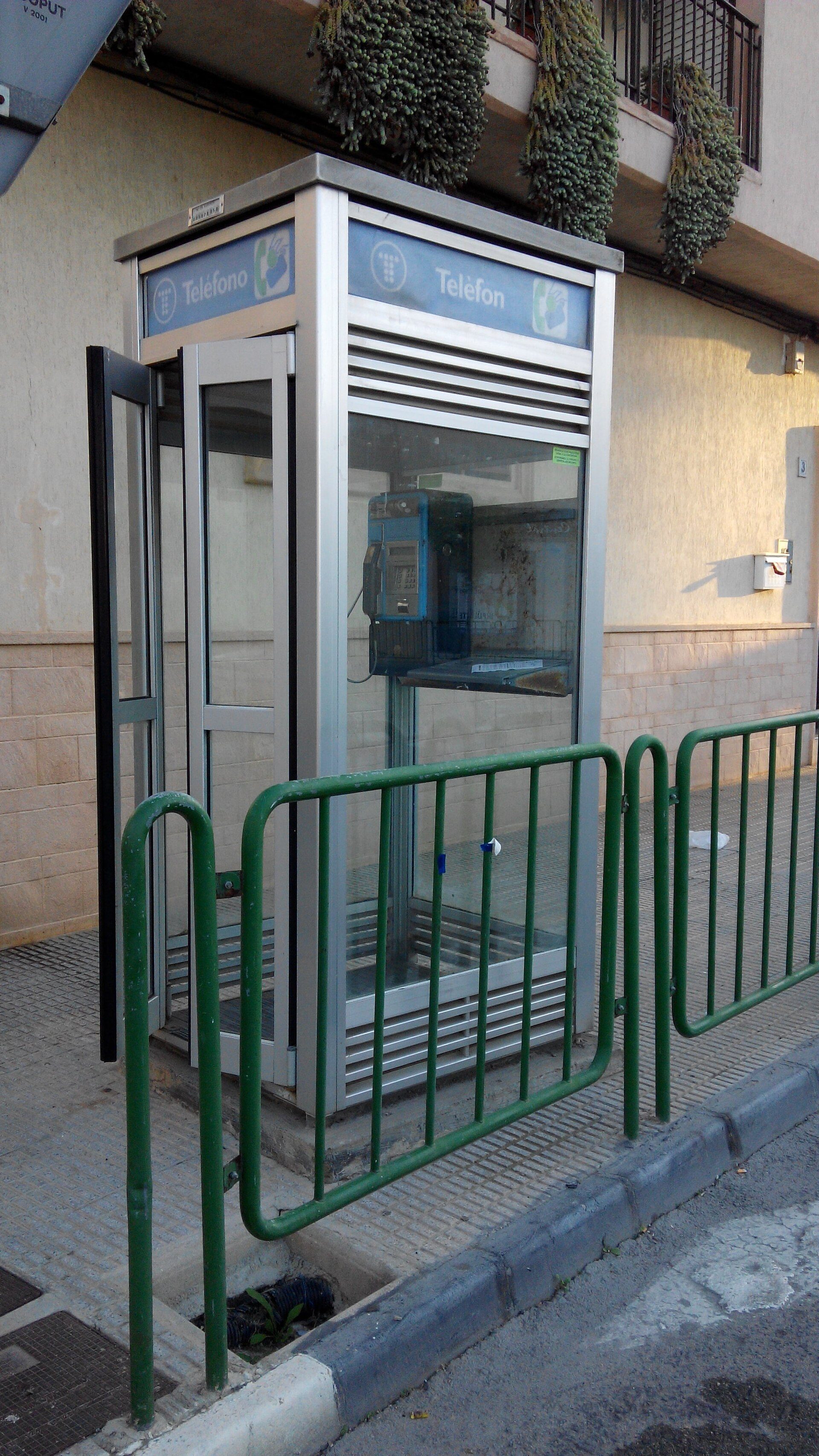 An outdoor Teléfonica payphone booth with glass doors and a metal frame.