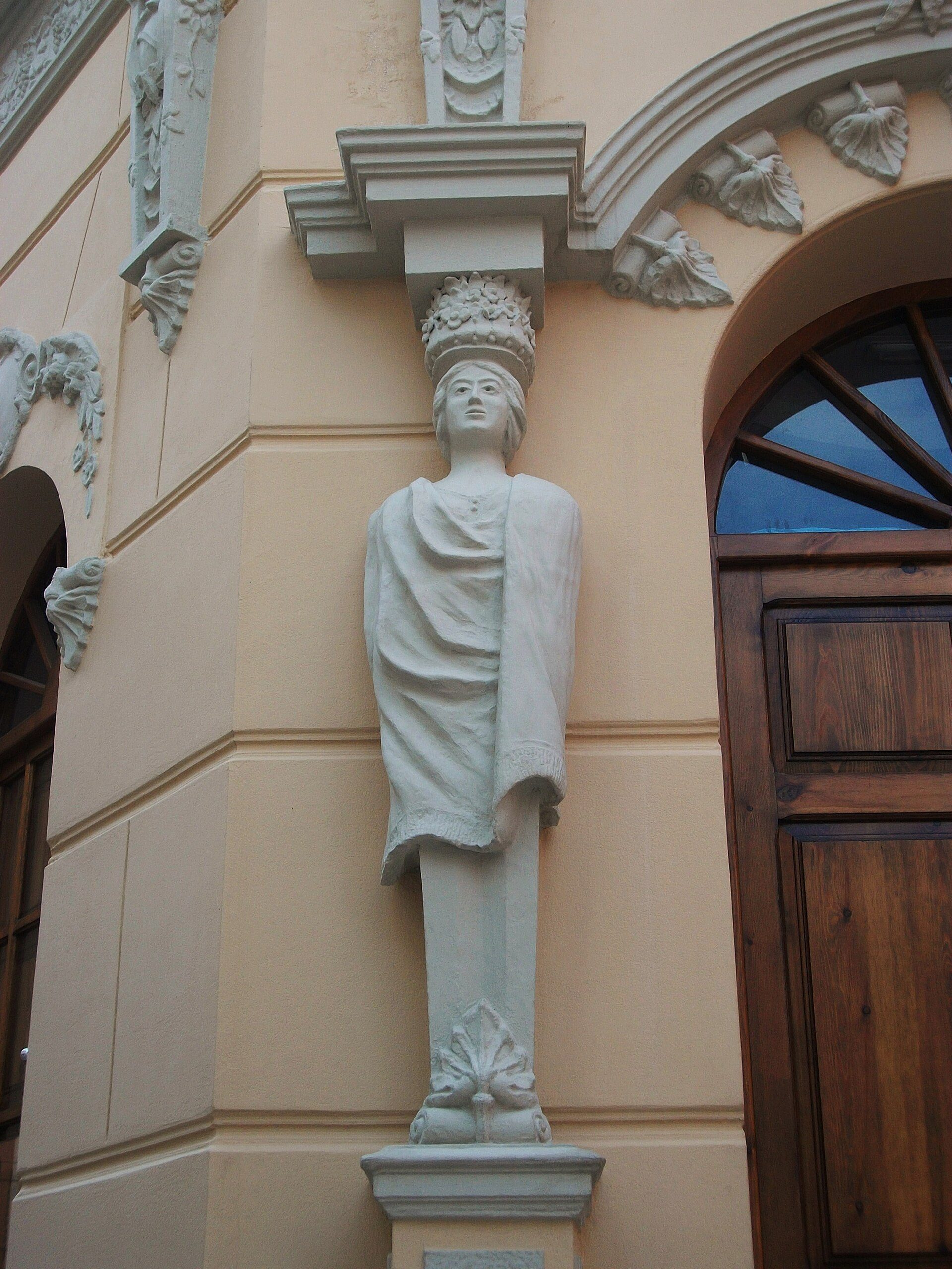 Alt text: Classical statue on a pedestal beside a wooden door with decorative carvings.