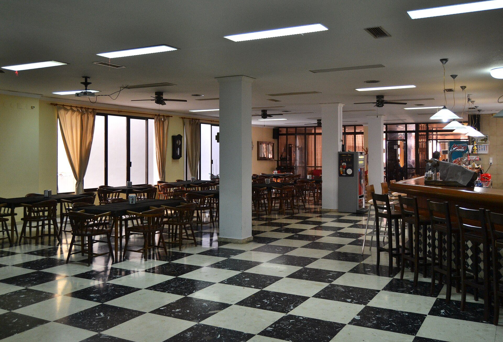 Alt text: Interior of a spacious dining room with checkered floor, large windows, and a bar area.