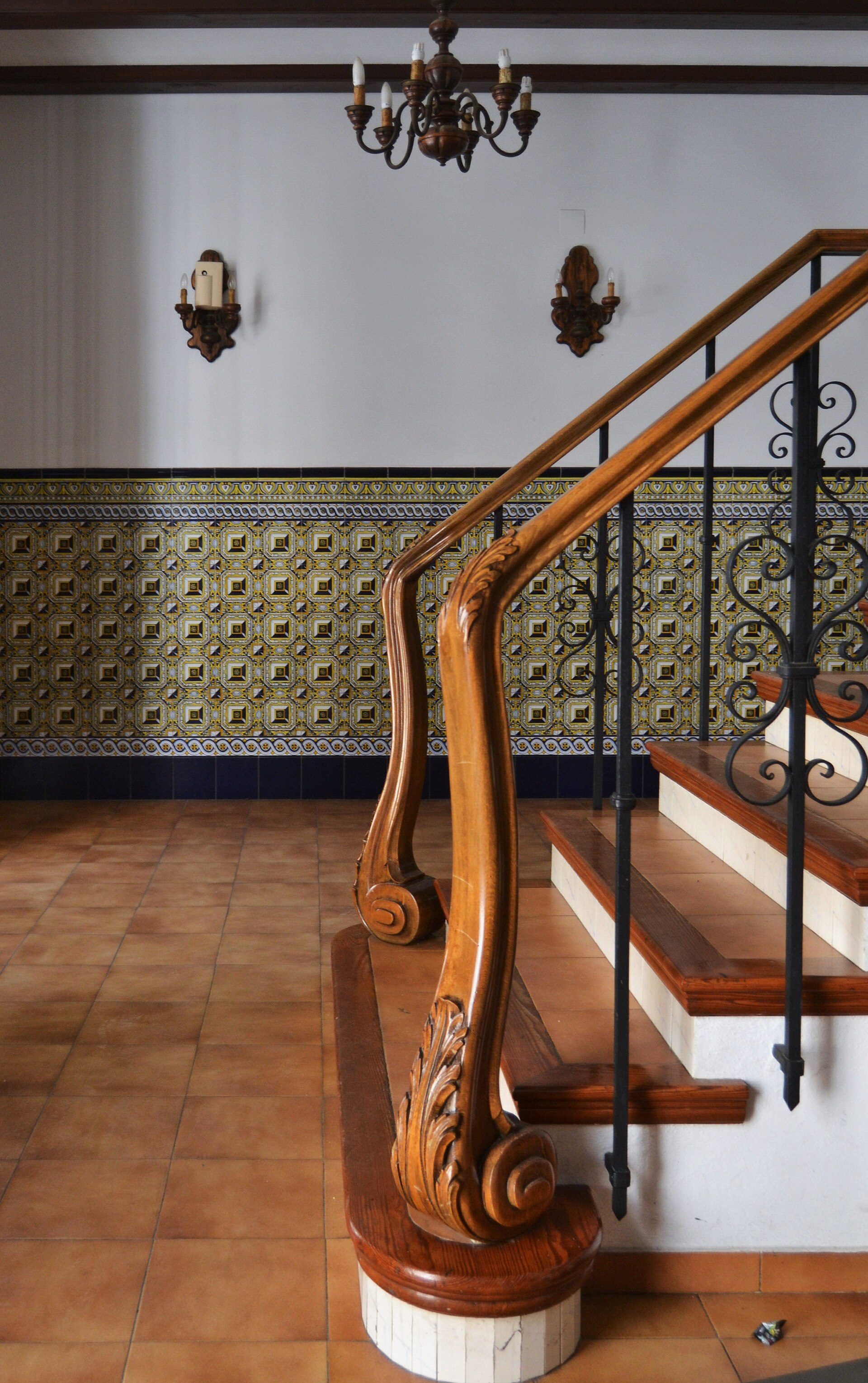 Interior view of a spacious room with a wooden staircase, chandelier, and patterned tile wall.