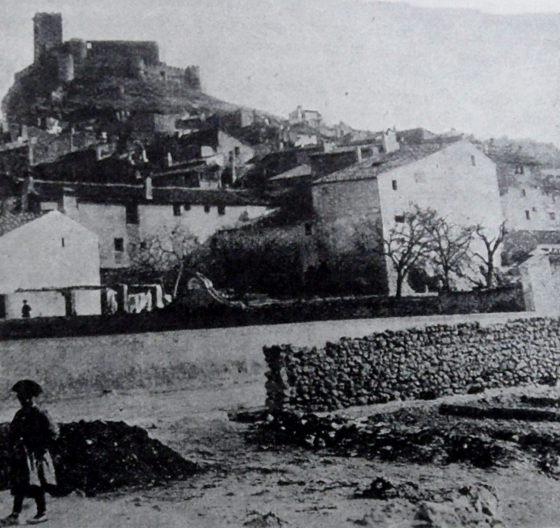 Alt text: Vintage photo of a hillside village with stone buildings and a castle view.