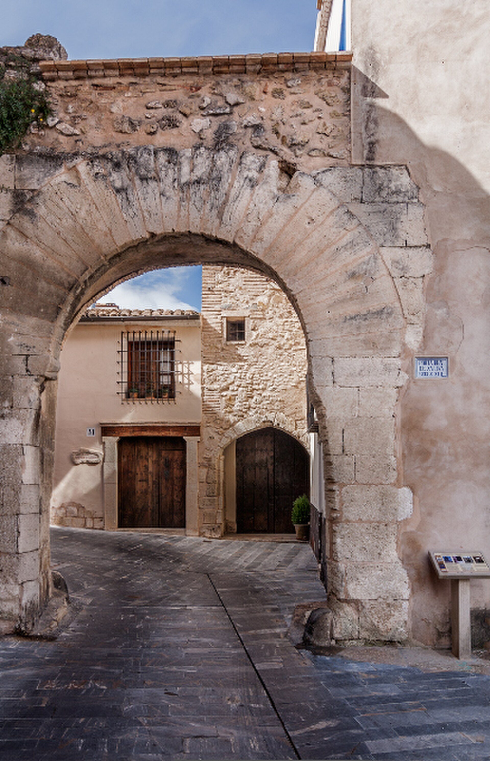 Traditional stone archway leading to a cozy courtyard with rustic doors and windows.