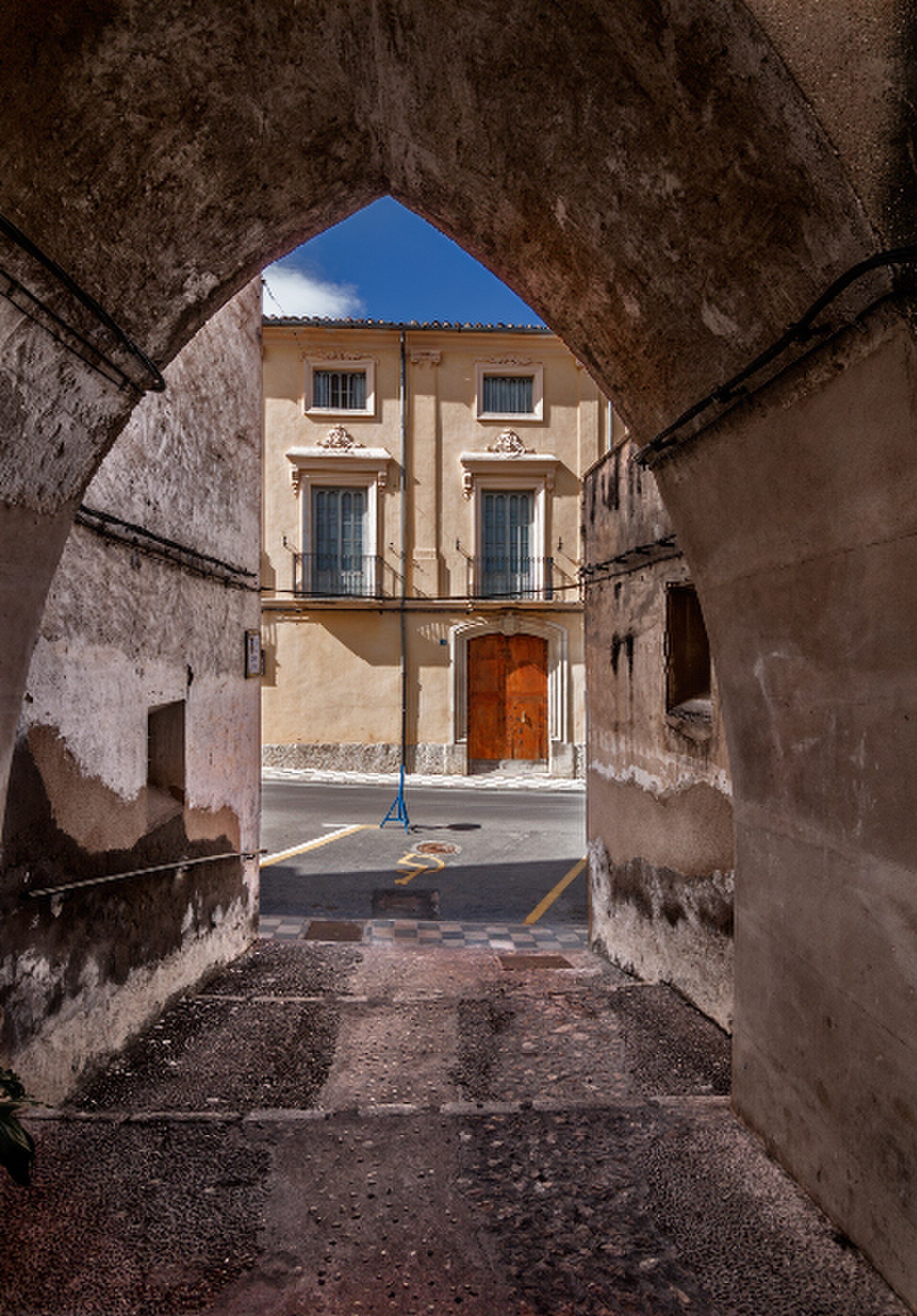 A sunlit courtyard with a view of a three-story building, featuring a central wooden door and balconies.