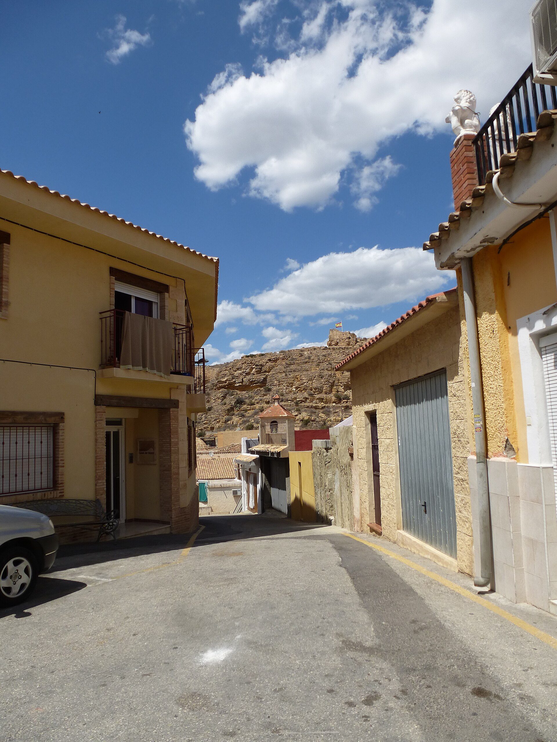 Two-story house with balcony, street view, yellow exterior, mountain backdrop.