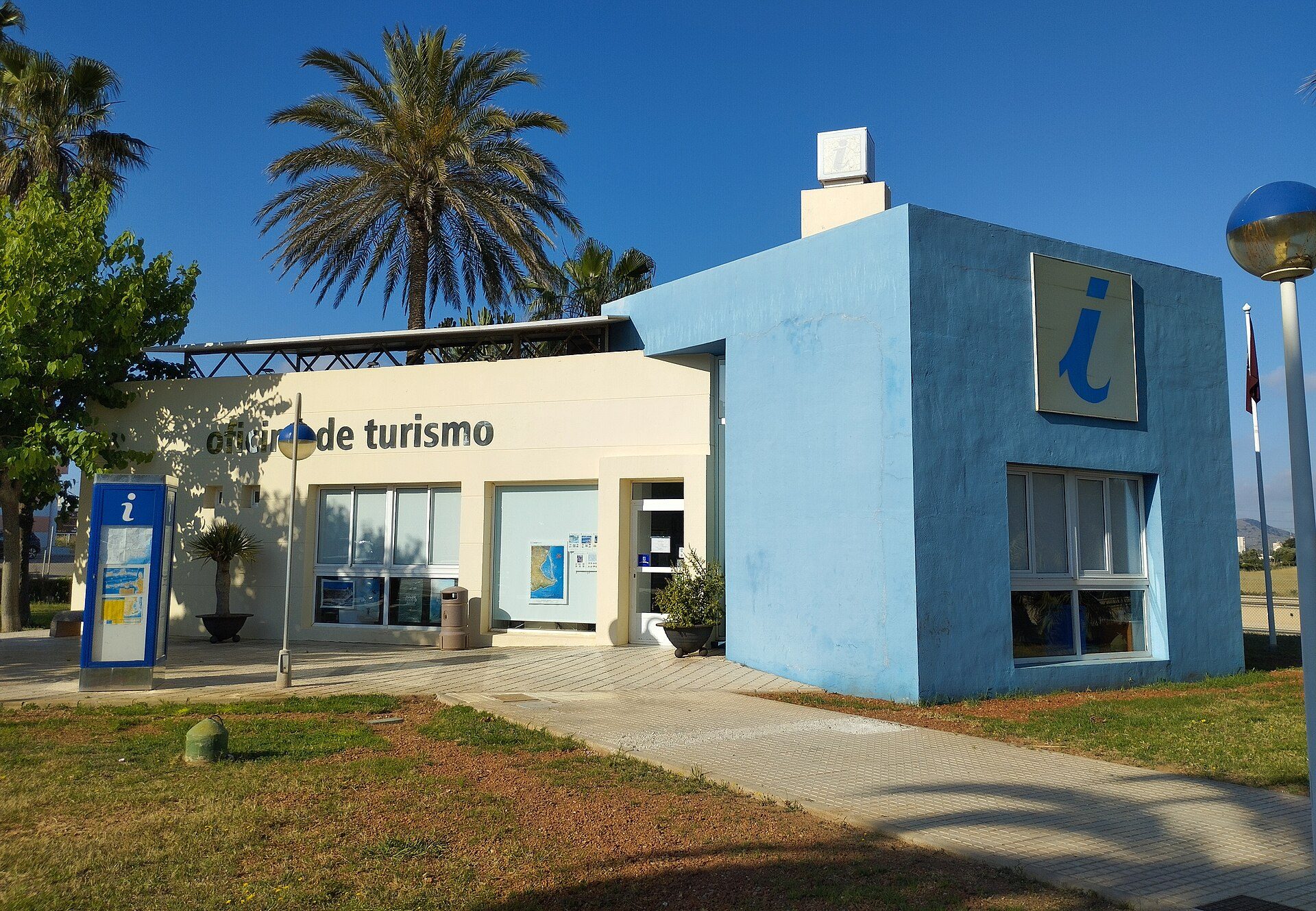 A blue and white building with a "i" sign, palm trees, and a clear blue sky.