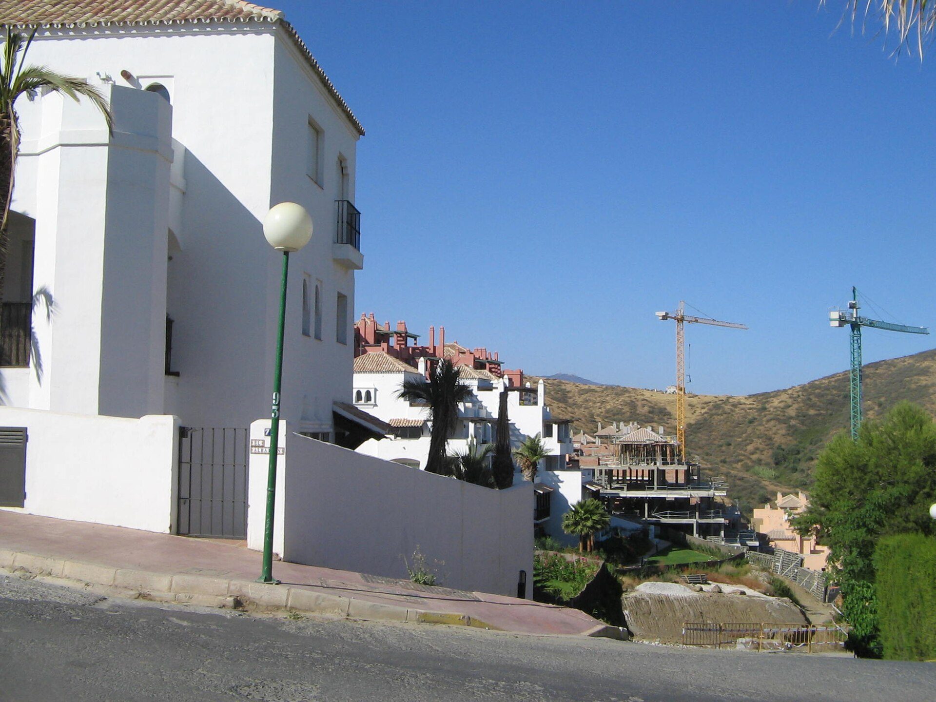 White building with balcony, scenic mountain view, construction cranes in background.