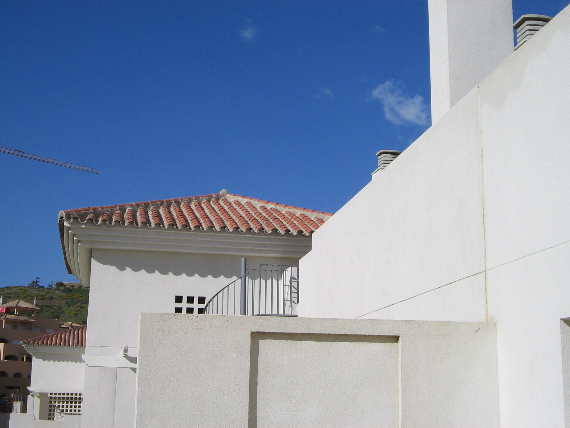 White building with red-tiled roof, balcony, and clear blue sky view.