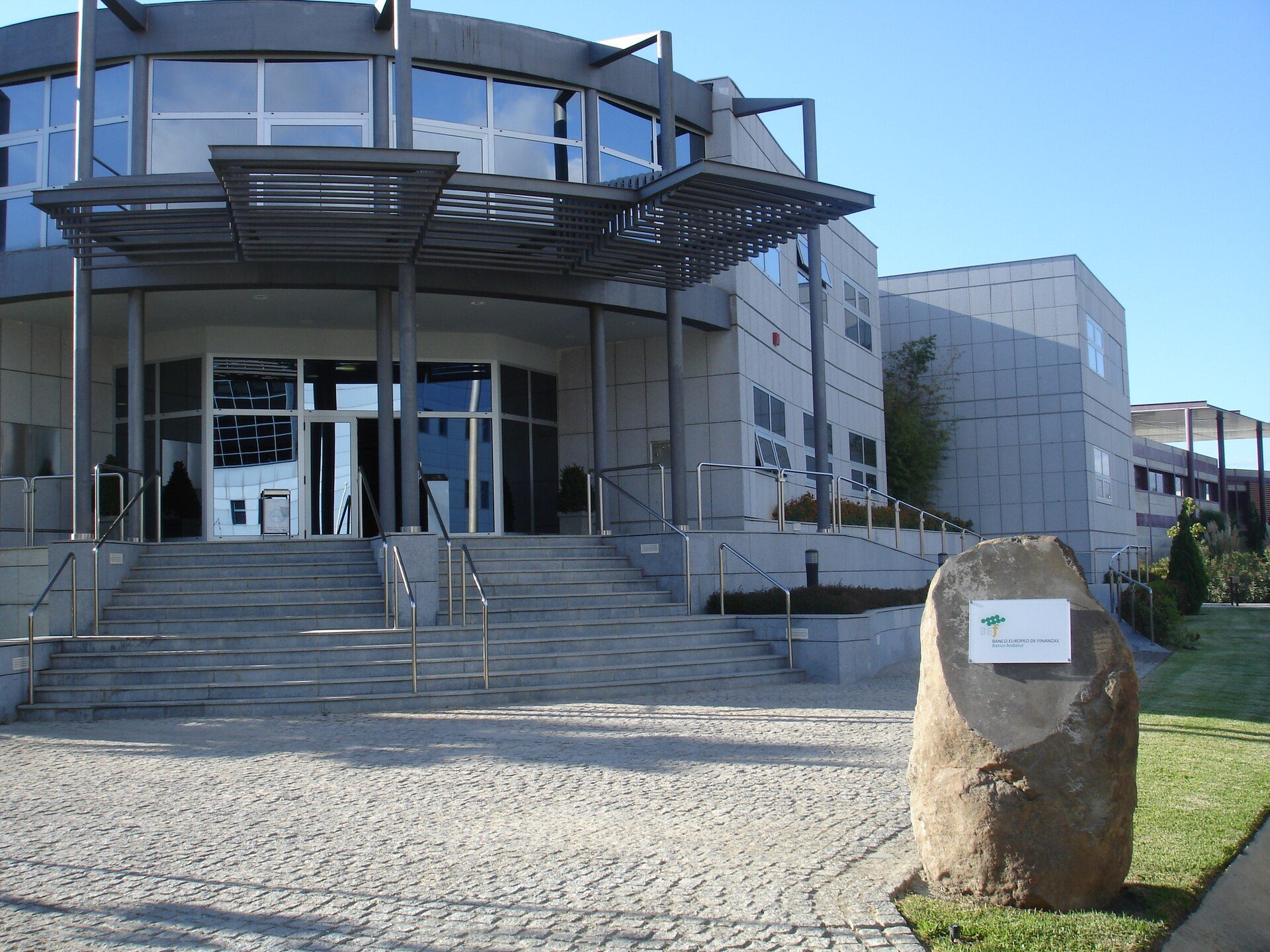 Modern office building with glass facade, stairs, and landscaped area.