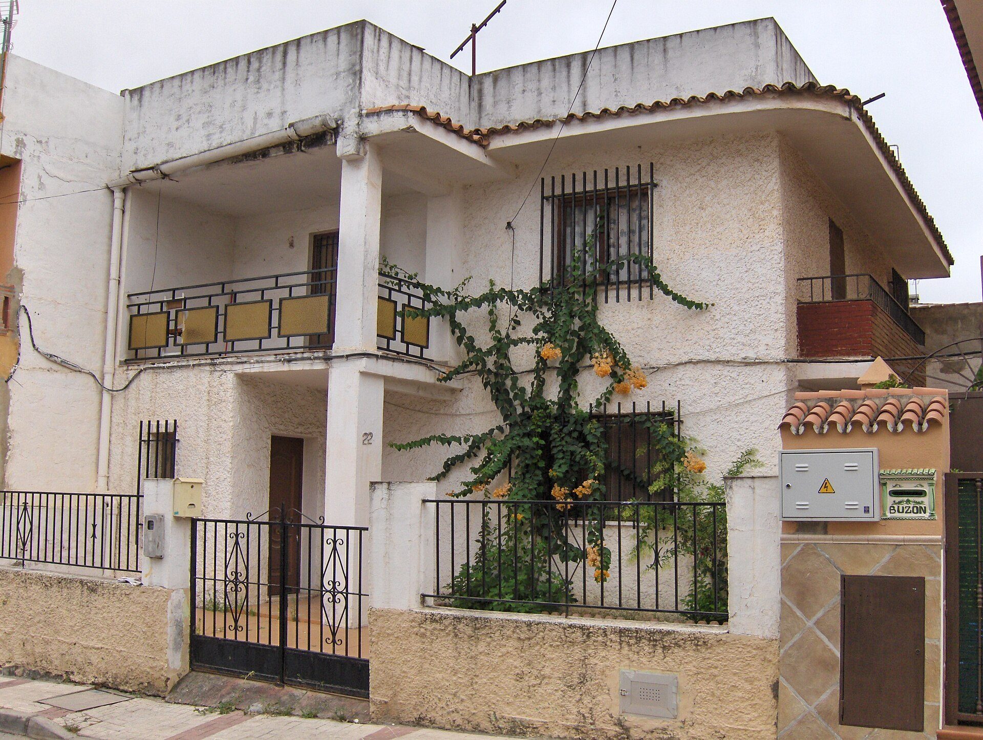 Two-story house with balcony, orange tree, and tiled roof.