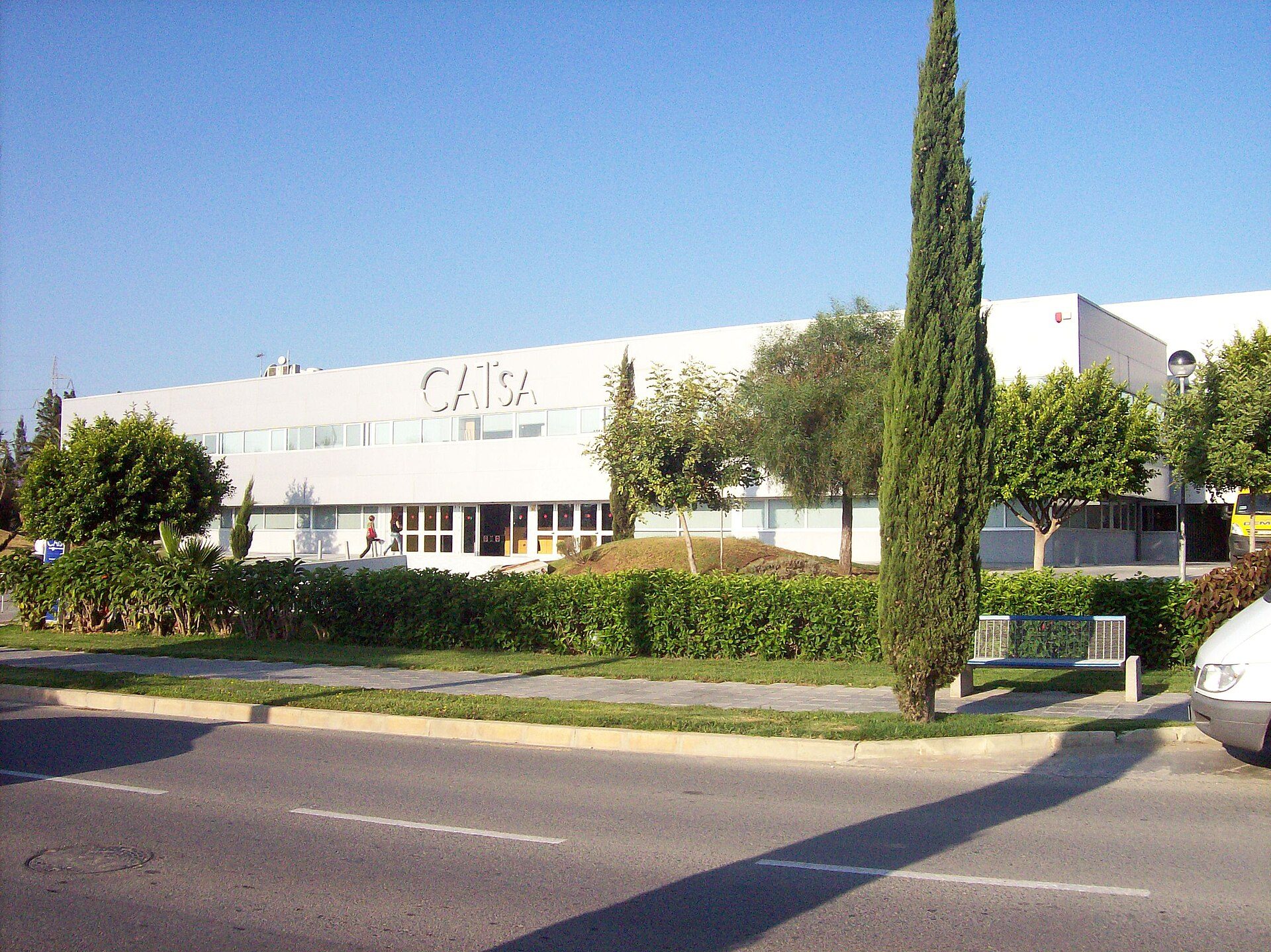 Modern office building with large windows, greenery, and a clear blue sky view.