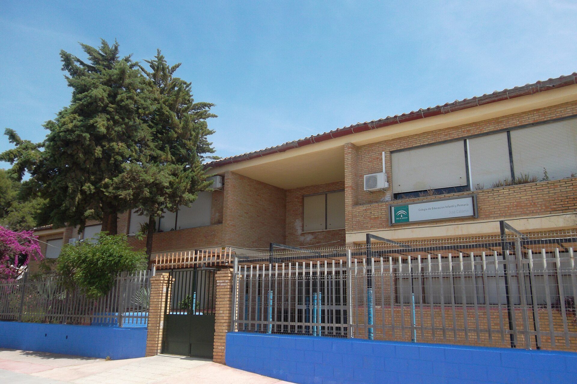 A two-story brick building with a fenced yard, large windows, and a tree.