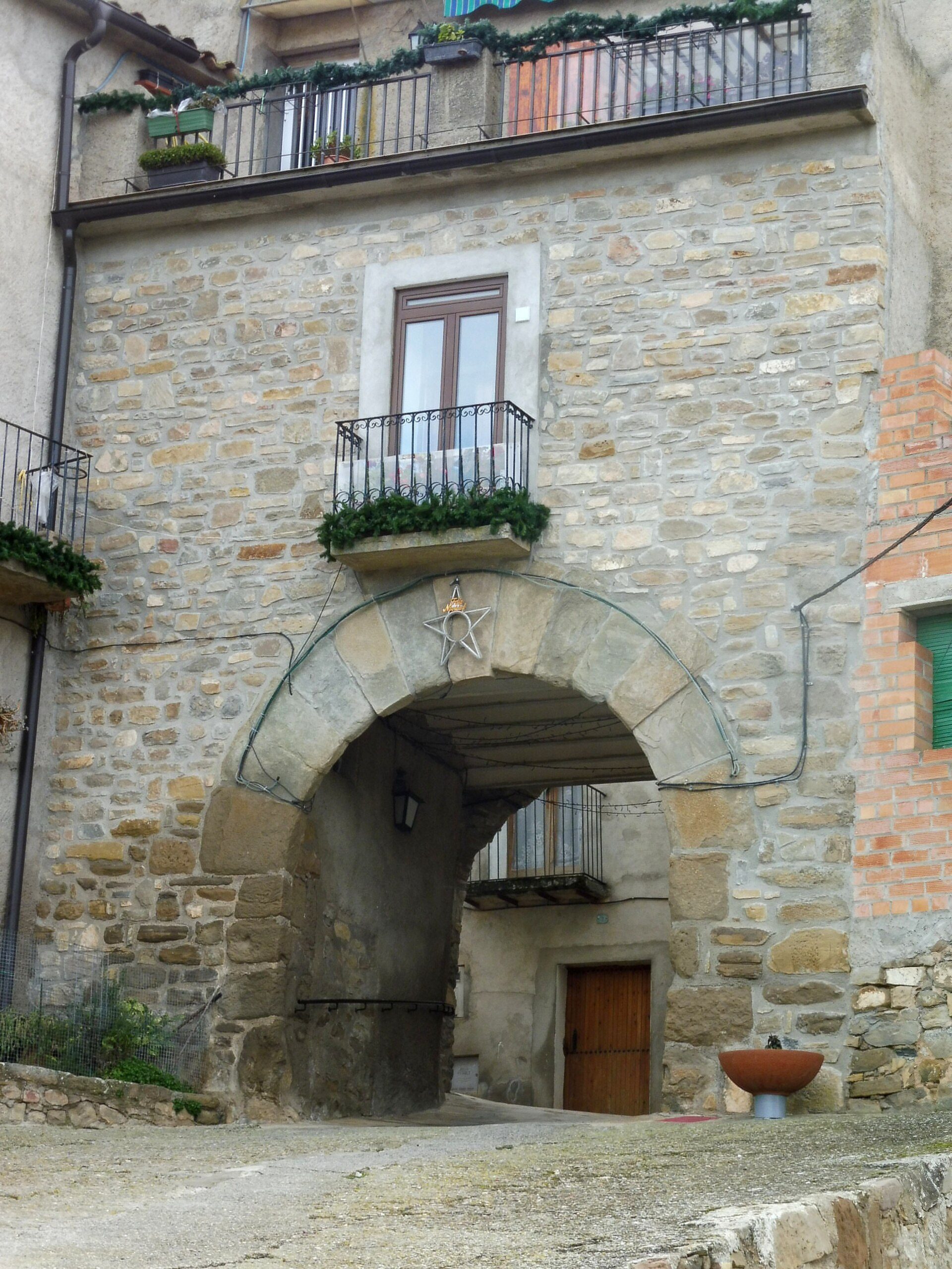 Alt text: Stone archway entrance with balcony, wooden door, and small garden.