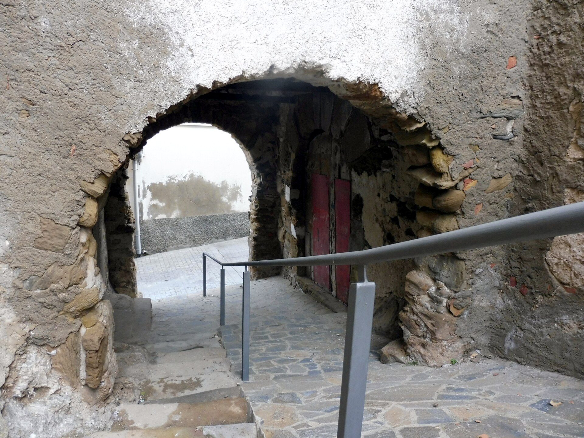 Stone archway leading to a courtyard with a red door and stone pathway.