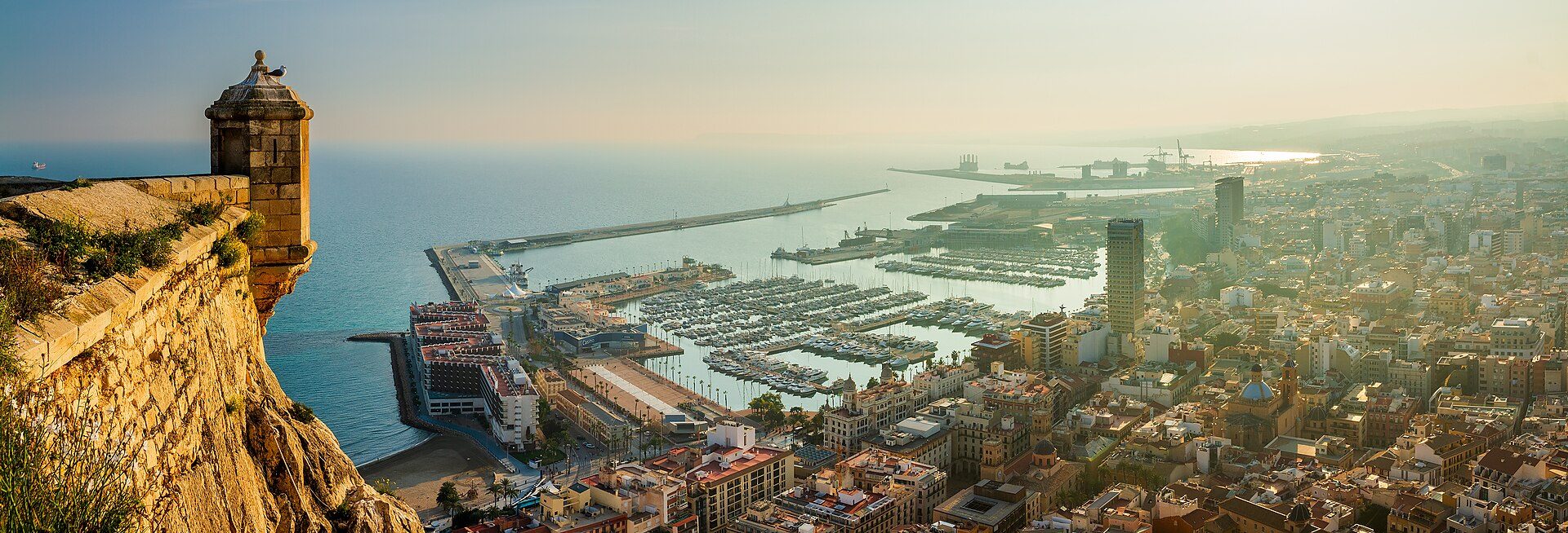 Aerial view of a coastal city with a harbor, cliffs, and a mix of modern and historic buildings.