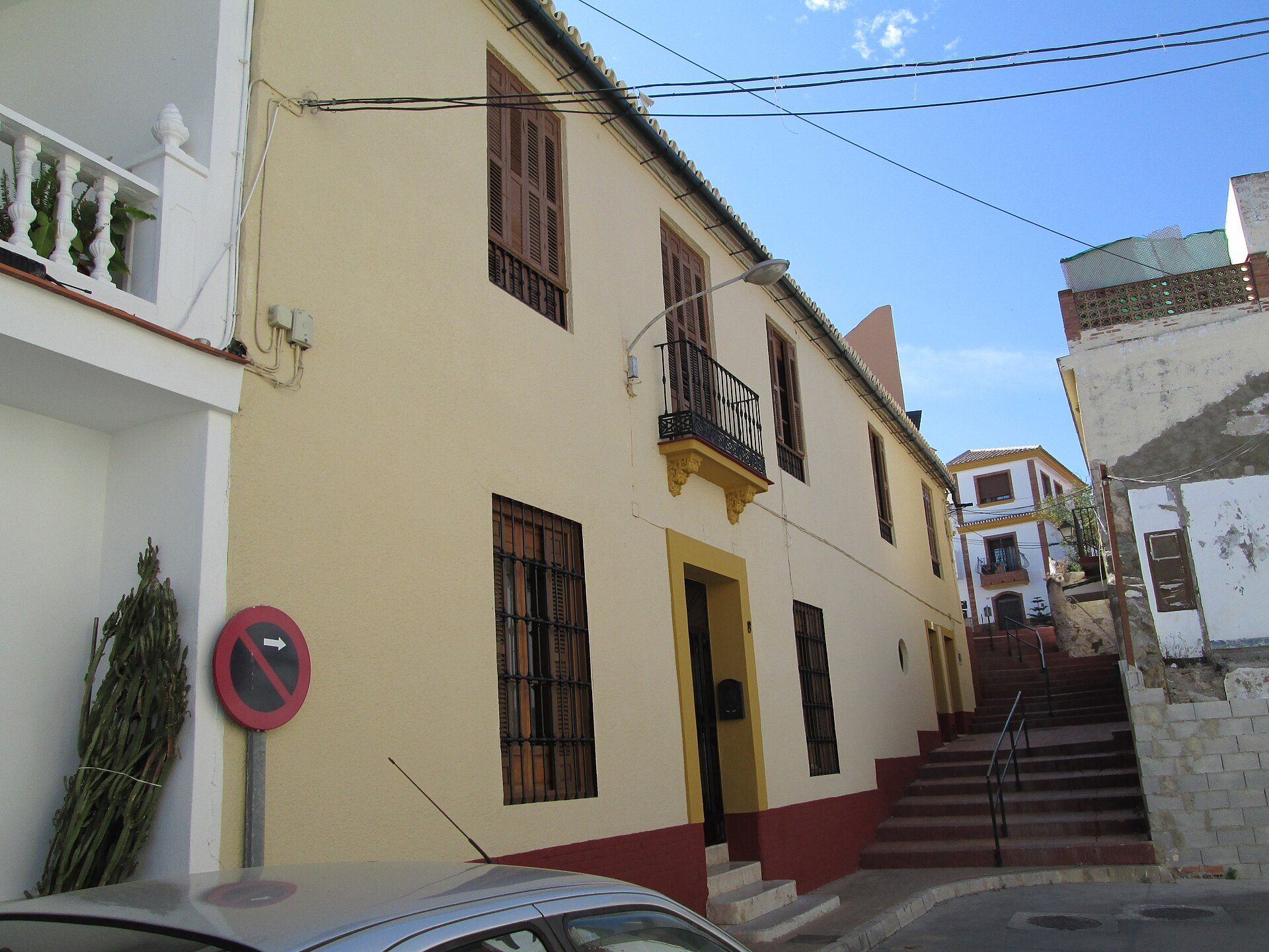 Two-story house with balcony, street view, yellow and red exterior.