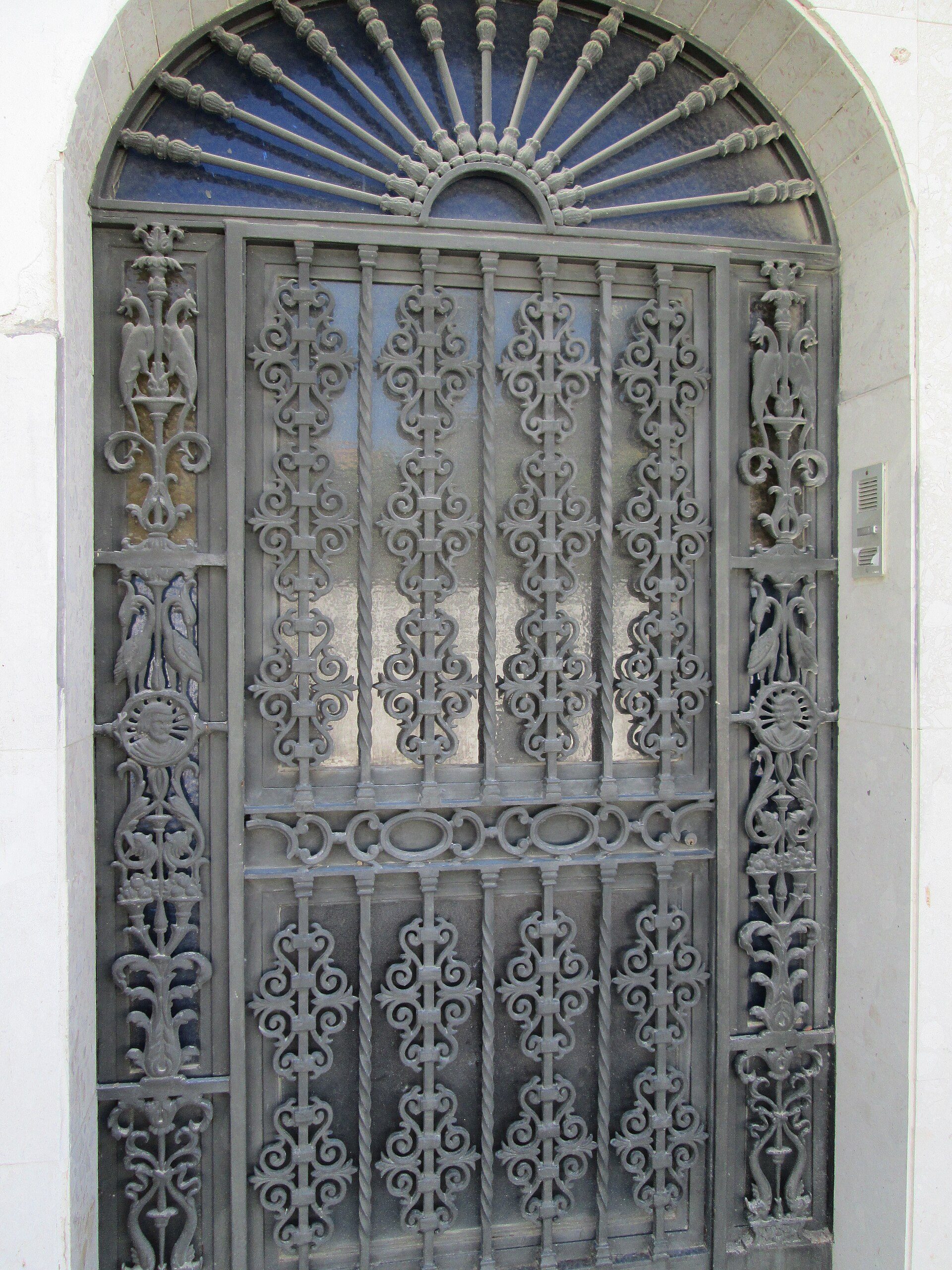 Elegant wrought iron door with intricate designs, leading to a spacious room with a balcony view.