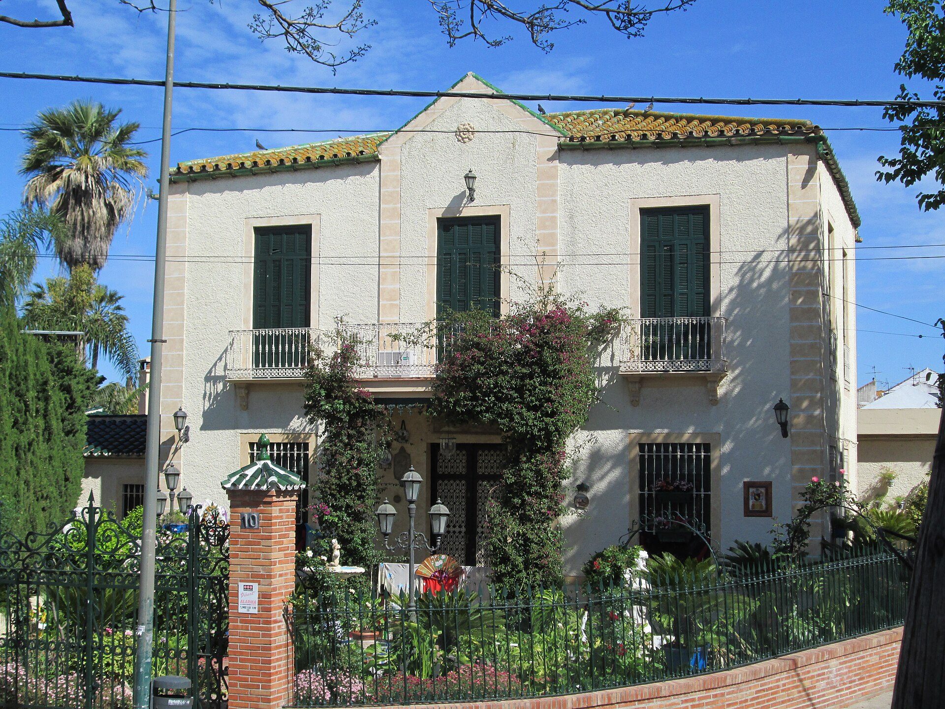 Two-story house with balcony, green shutters, and garden view.