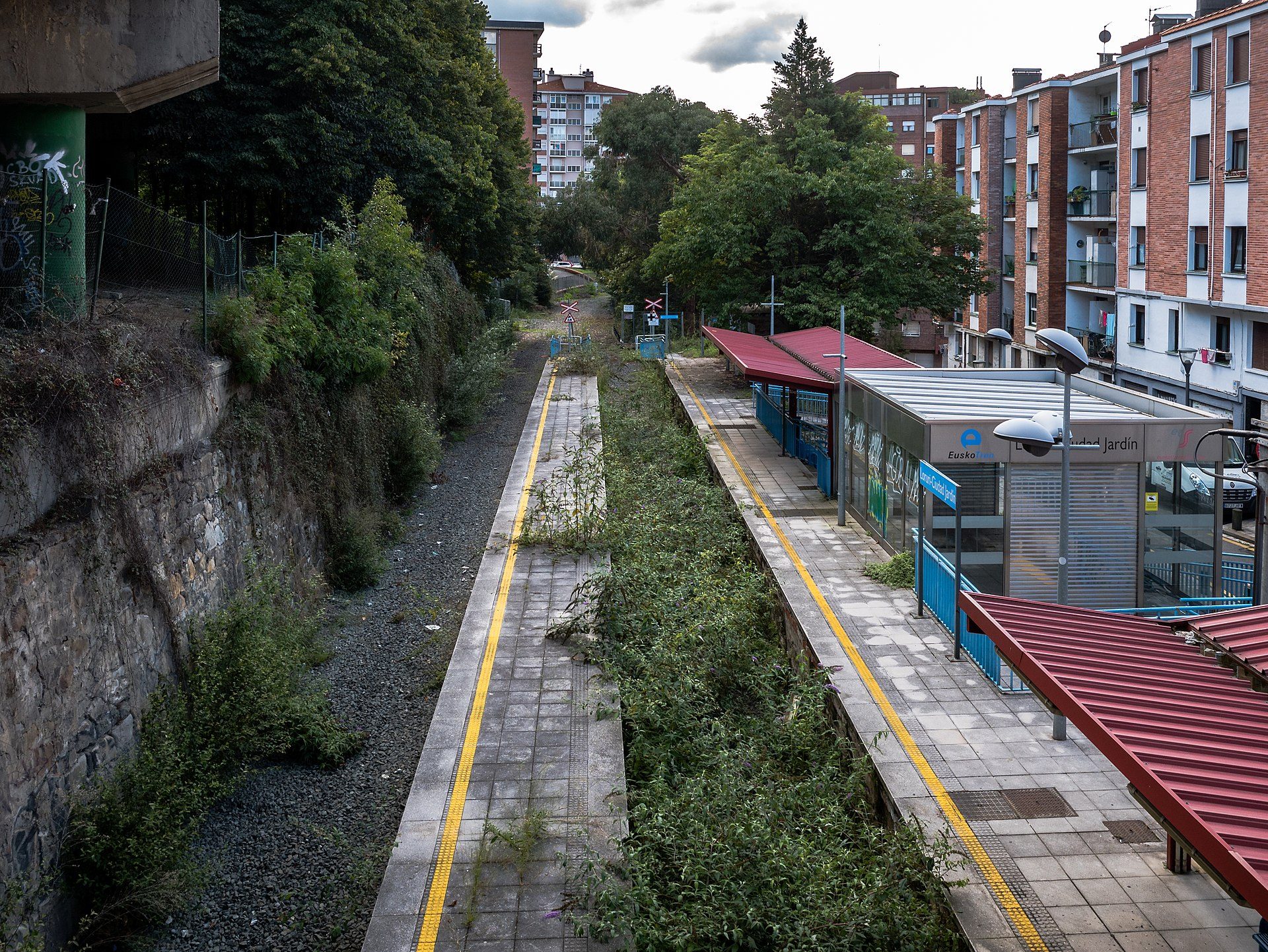 Alt text: "Railway track view with modern buildings and greenery on both sides.